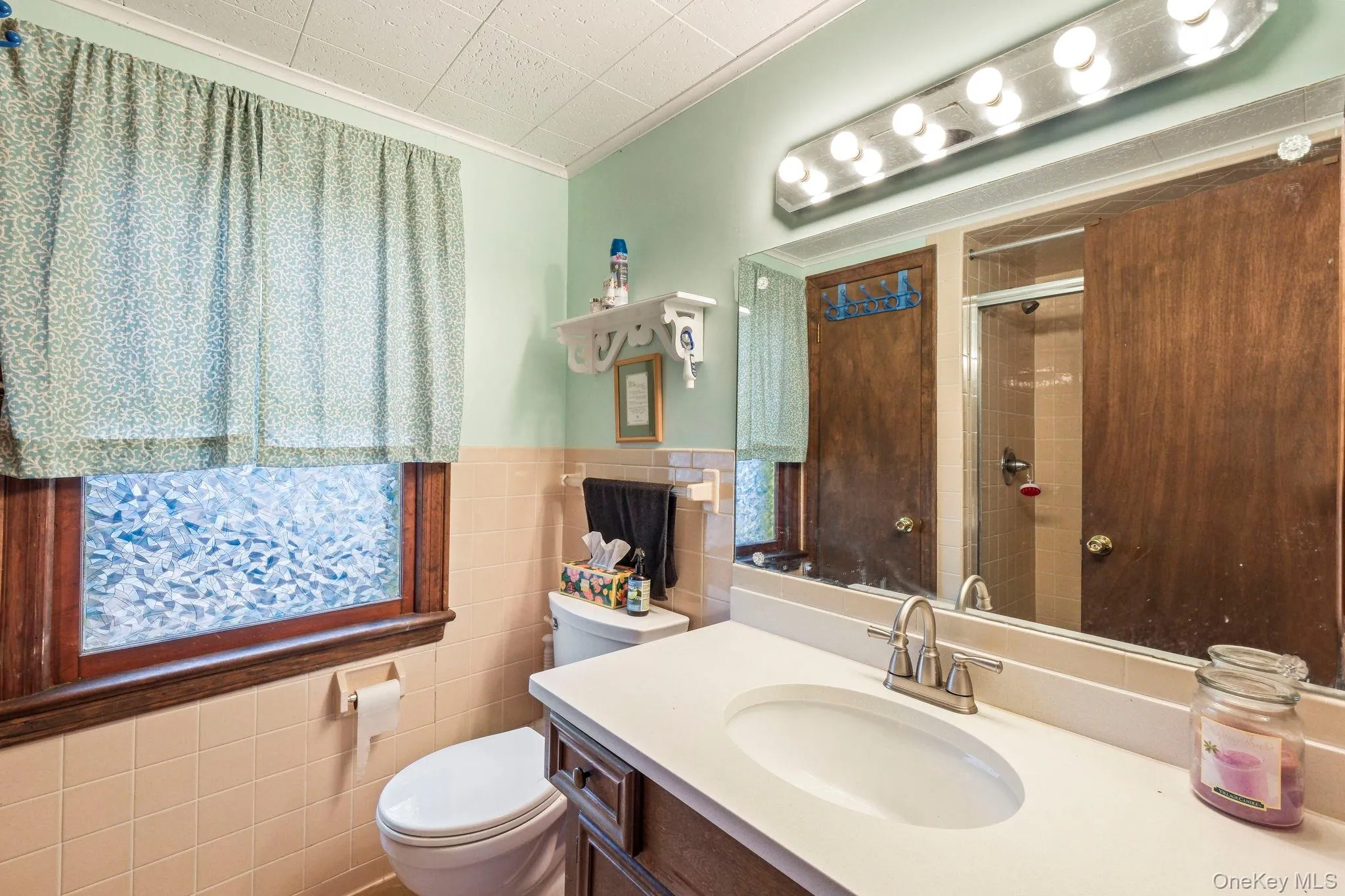 Bathroom with vanity, tile walls, crown molding, a stall shower, and a wainscoted wall Bathroom with vanity, tile walls, crown molding, a stall shower, and a wainscoted wall