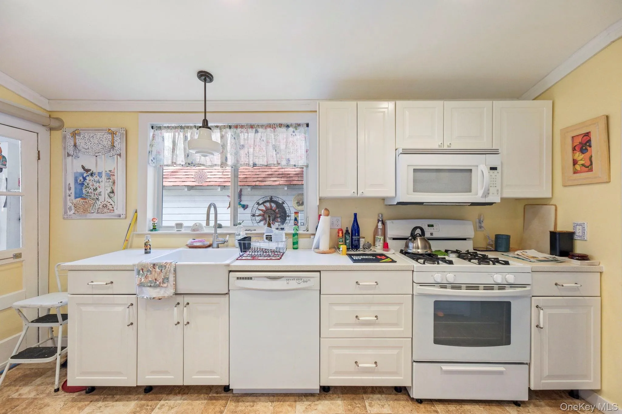 Kitchen with ornamental molding, white appliances, light countertops, decorative light fixtures, and white cabinets Kitchen with ornamental molding, white appliances, light countertops, decorative light fixtures, and white cabinets