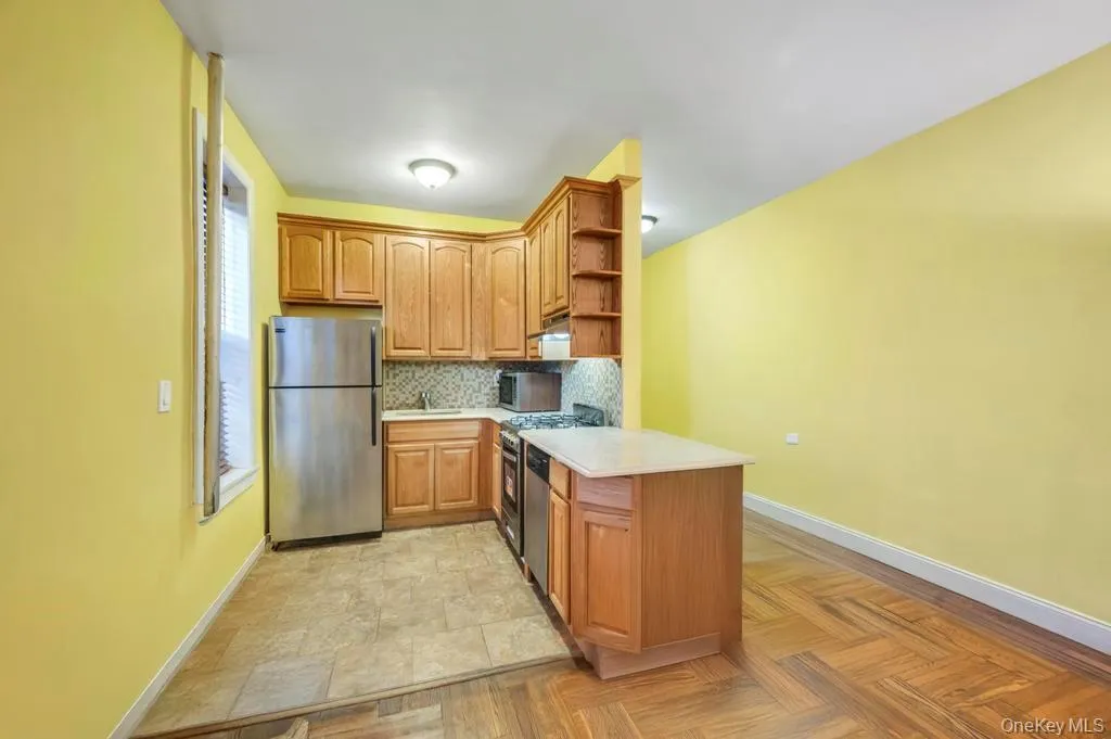 Kitchen featuring appliances with stainless steel finishes, open shelves, backsplash, brown cabinetry, and a peninsula/ kitchen bar. Kitchen featuring appliances with stainless steel finishes, open shelves, backsplash, brown cabinetry, and a peninsula/ kitchen bar.