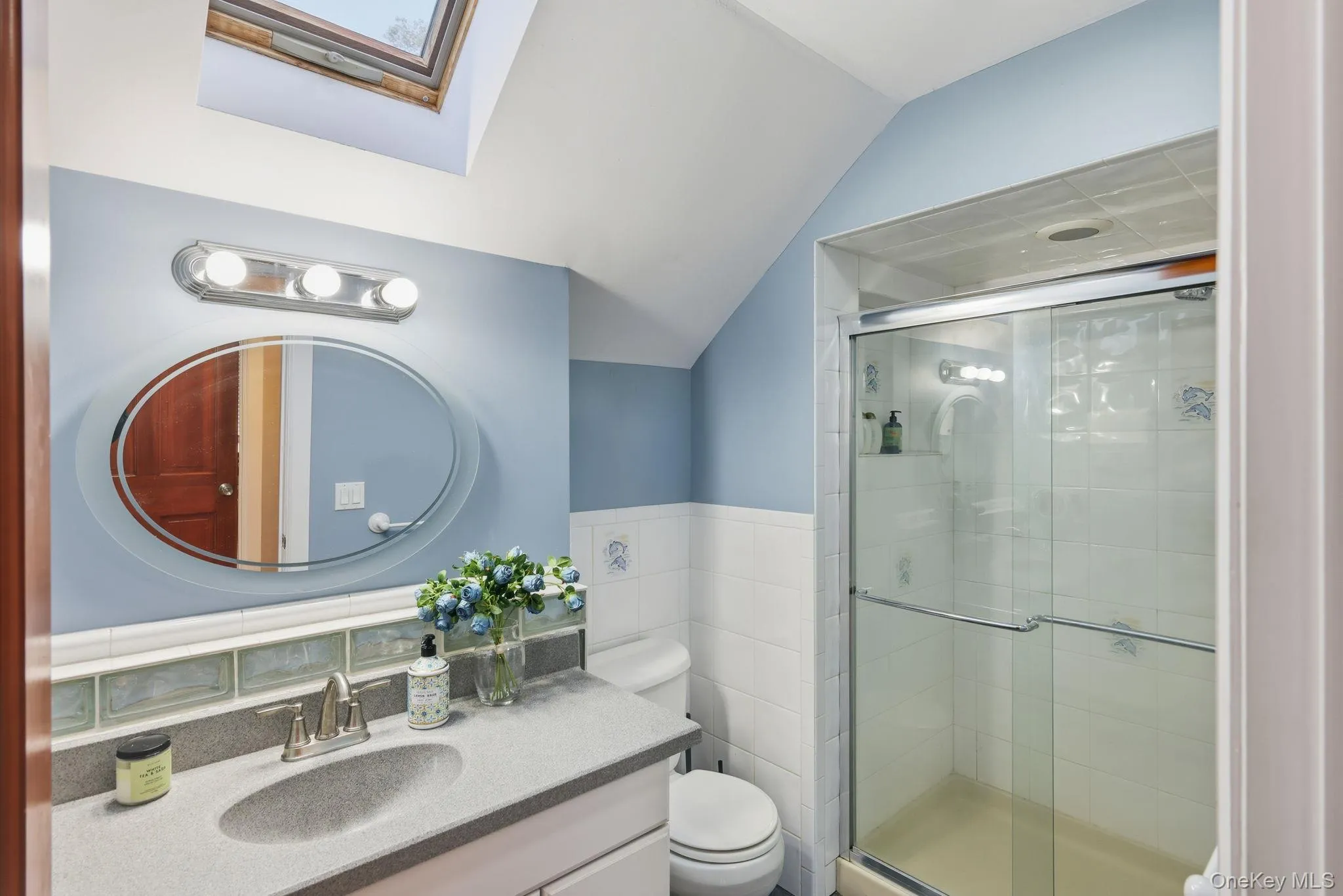 Full bathroom with vanity, a skylight, vaulted ceiling, a shower stall, and tile walls Full bathroom with vanity, a skylight, vaulted ceiling, a shower stall, and tile walls