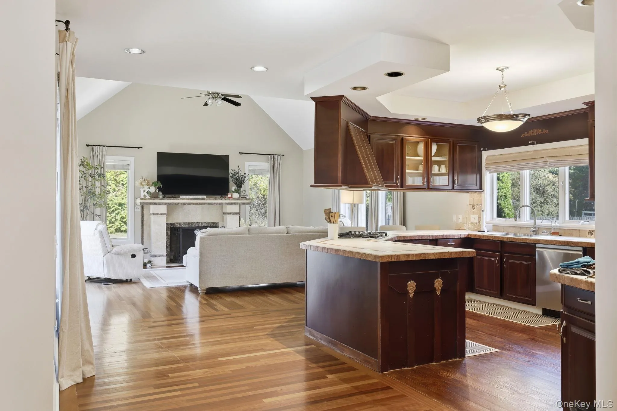 Kitchen with dark wood-style floors, decorative light fixtures, lofted ceiling, glass insert cabinets, and dark brown cabinetry Kitchen with dark wood-style floors, decorative light fixtures, lofted ceiling, glass insert cabinets, and dark brown cabinetry