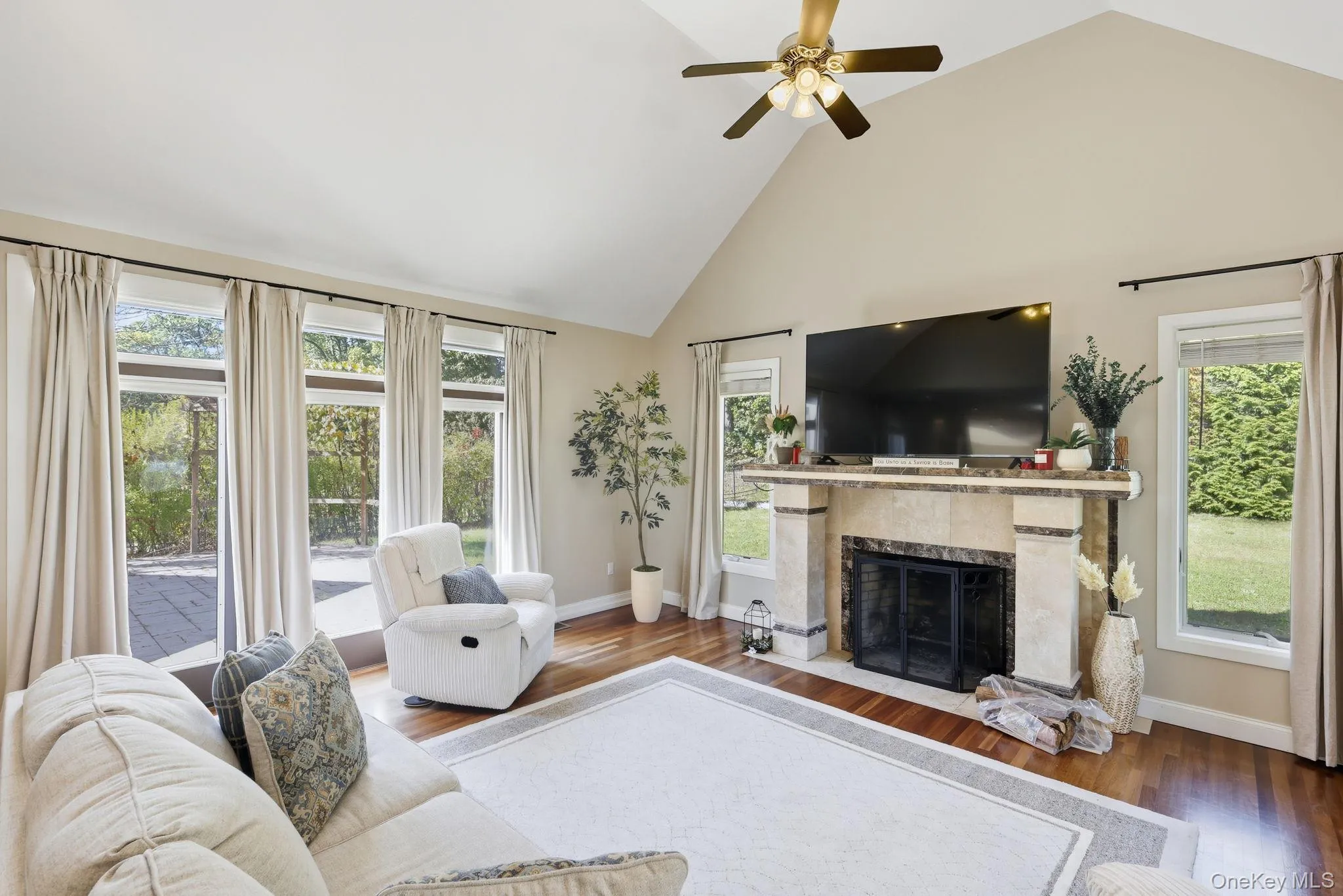 Living area featuring high vaulted ceiling, plenty of natural light, wood finished floors, a high end fireplace, and ceiling fan Living area featuring high vaulted ceiling, plenty of natural light, wood finished floors, a high end fireplace, and ceiling fan