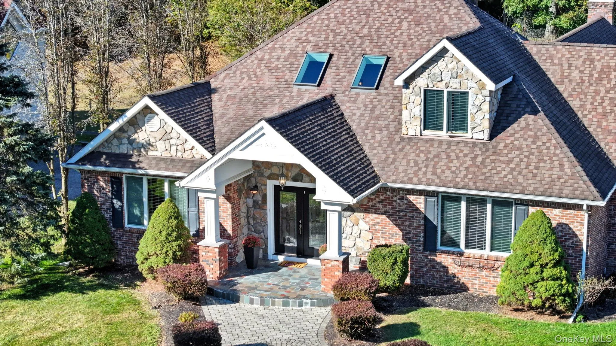 View of front of home featuring roof with shingles, stone siding, a front lawn, and brick siding View of front of home featuring roof with shingles, stone siding, a front lawn, and brick siding