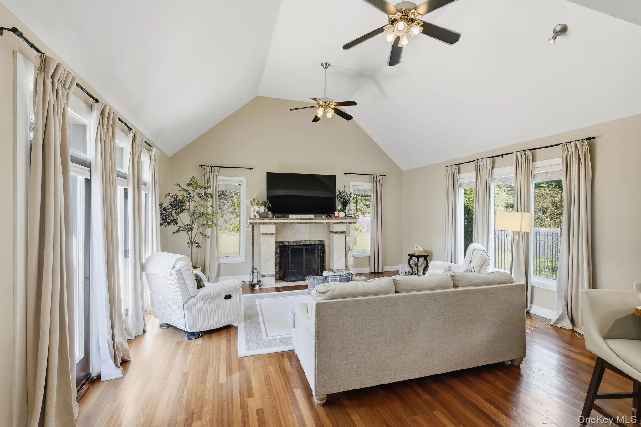 Living area with a high end fireplace, wood finished floors, a ceiling fan, and high vaulted ceiling Living area with a high end fireplace, wood finished floors, a ceiling fan, and high vaulted ceiling