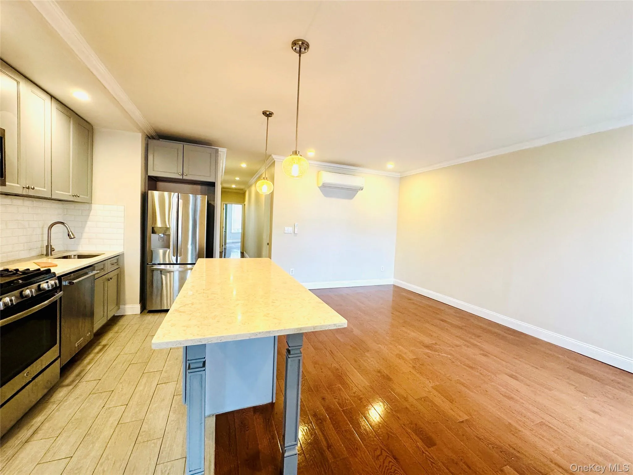 Kitchen with tasteful backsplash, crown molding, gray cabinetry, pendant lighting, and appliances with stainless steel finishes Kitchen with tasteful backsplash, crown molding, gray cabinetry, pendant lighting, and appliances with stainless steel finishes