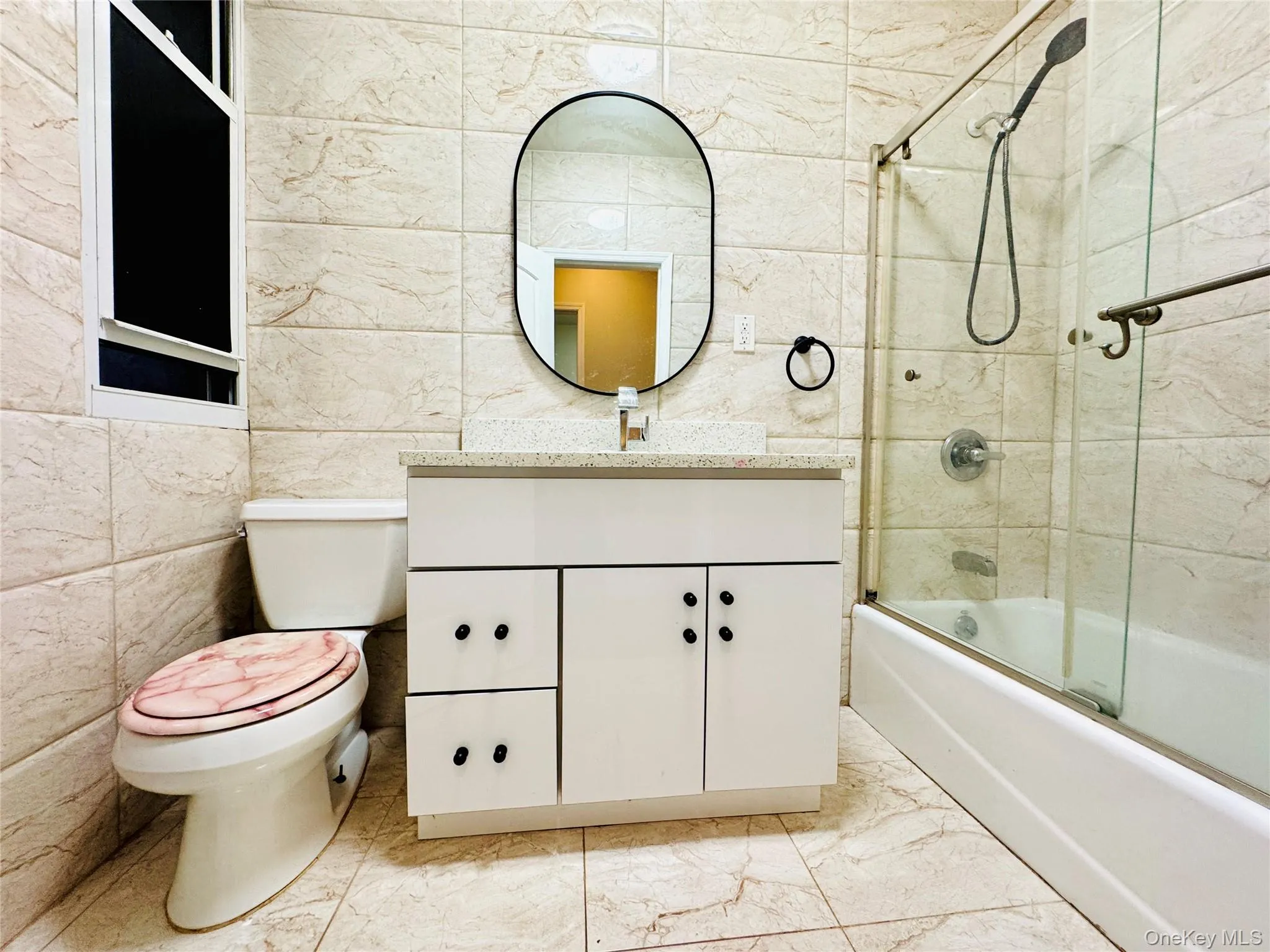 Full bath with vanity, combined bath / shower with glass door, light marble finish flooring, and tile walls Full bath with vanity, combined bath / shower with glass door, light marble finish flooring, and tile walls