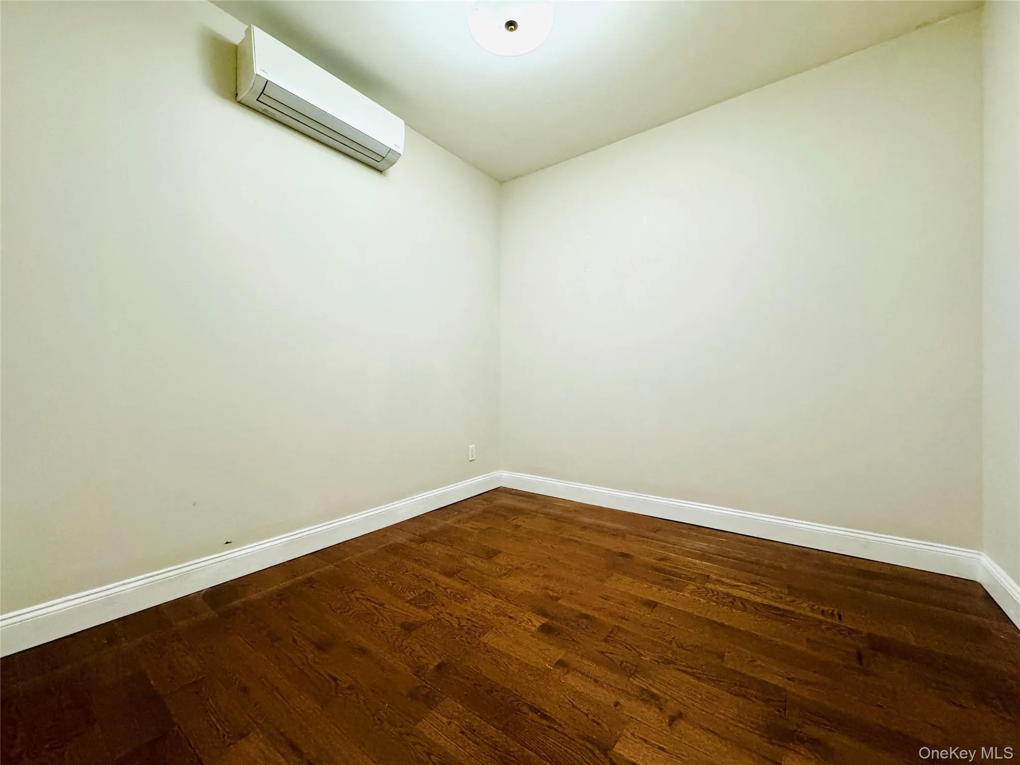 Empty room with dark wood-style floors and an AC wall unit Empty room with dark wood-style floors and an AC wall unit