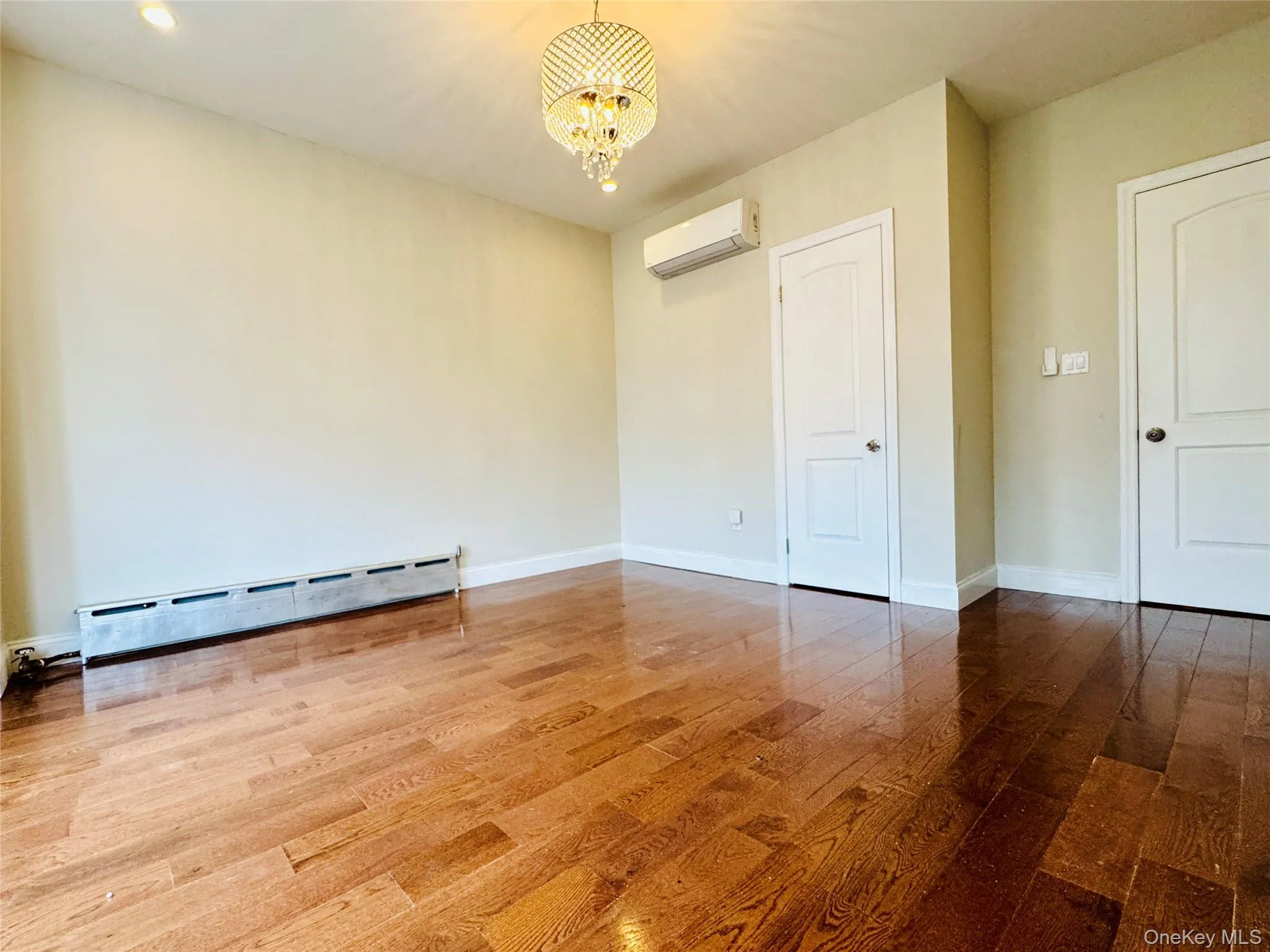 Unfurnished bedroom featuring wood finished floors, a baseboard heating unit, a chandelier, and a wall mounted AC Unfurnished bedroom featuring wood finished floors, a baseboard heating unit, a chandelier, and a wall mounted AC