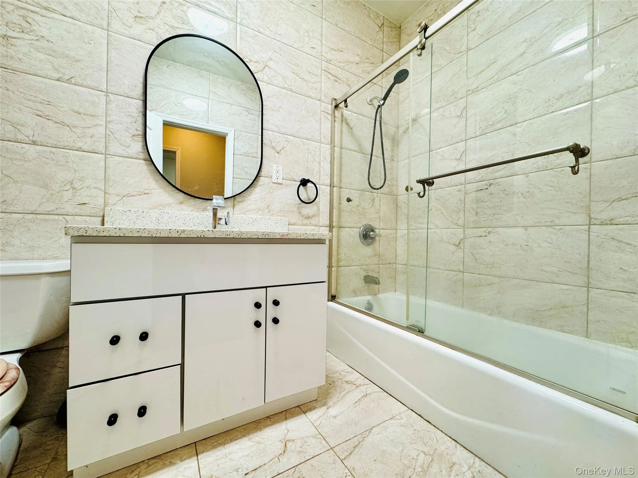 Bathroom featuring vanity, bath / shower combo with glass door, and light marble finish flooring Bathroom featuring vanity, bath / shower combo with glass door, and light marble finish flooring