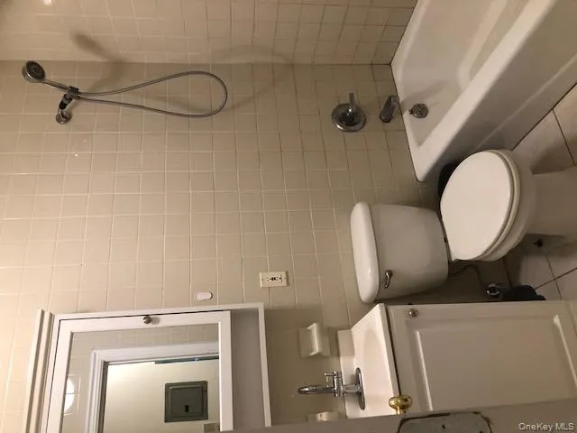 Full bathroom with tile walls, tile patterned flooring, shower combination, vanity, and electric panel Full bathroom with tile walls, tile patterned flooring, shower combination, vanity, and electric panel