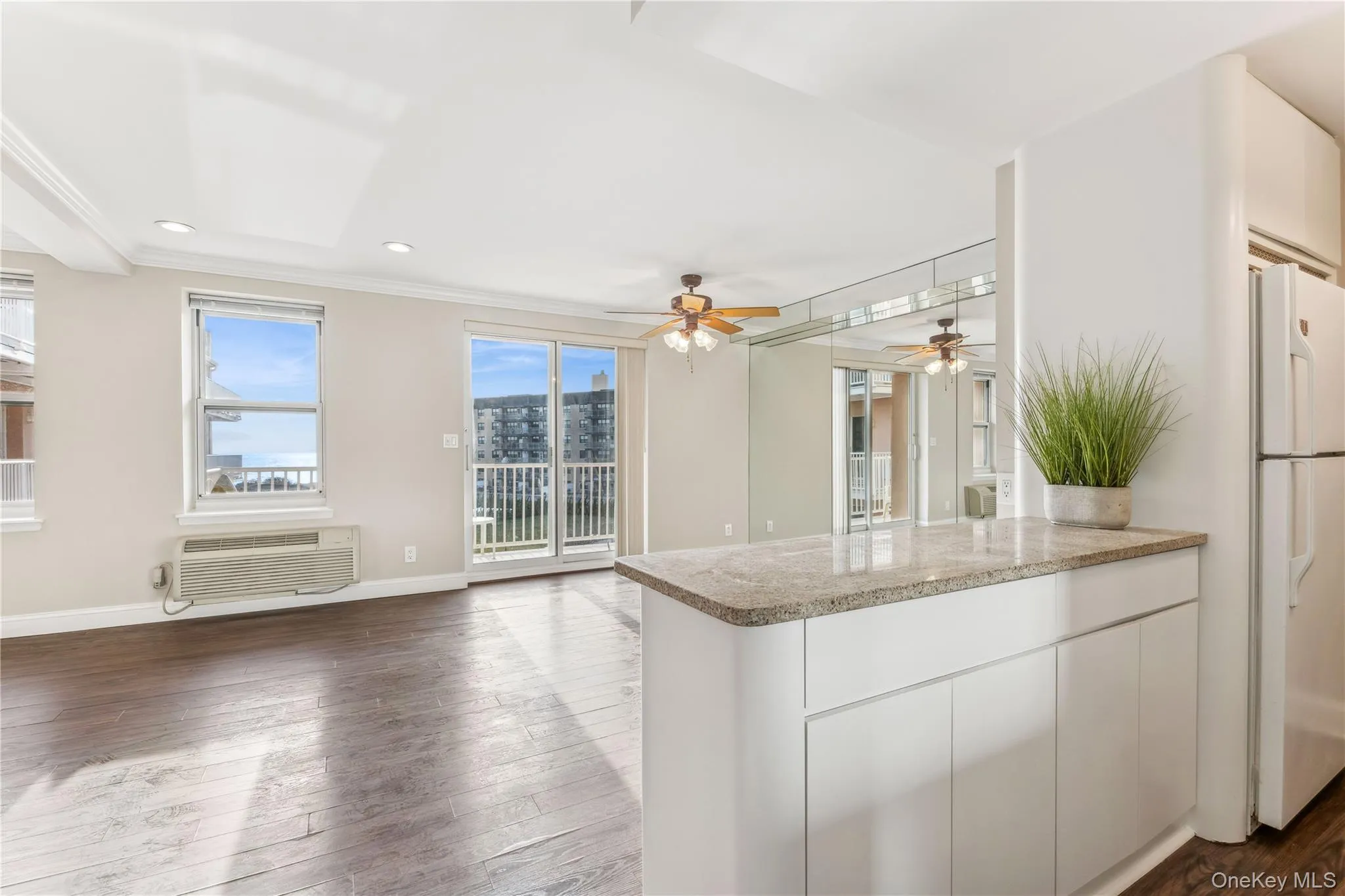 Kitchen featuring dark wood-type flooring, white cabinets, white refrigerator, a wall mounted AC, and light stone counters Kitchen featuring dark wood-type flooring, white cabinets, white refrigerator, a wall mounted AC, and light stone counters