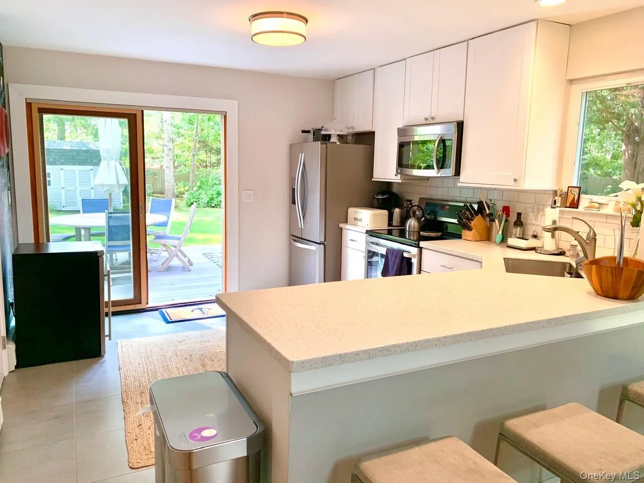 Kitchen featuring appliances with stainless steel finishes, backsplash, a kitchen breakfast bar, a peninsula, and white cabinetry Kitchen featuring appliances with stainless steel finishes, backsplash, a kitchen breakfast bar, a peninsula, and white cabinetry