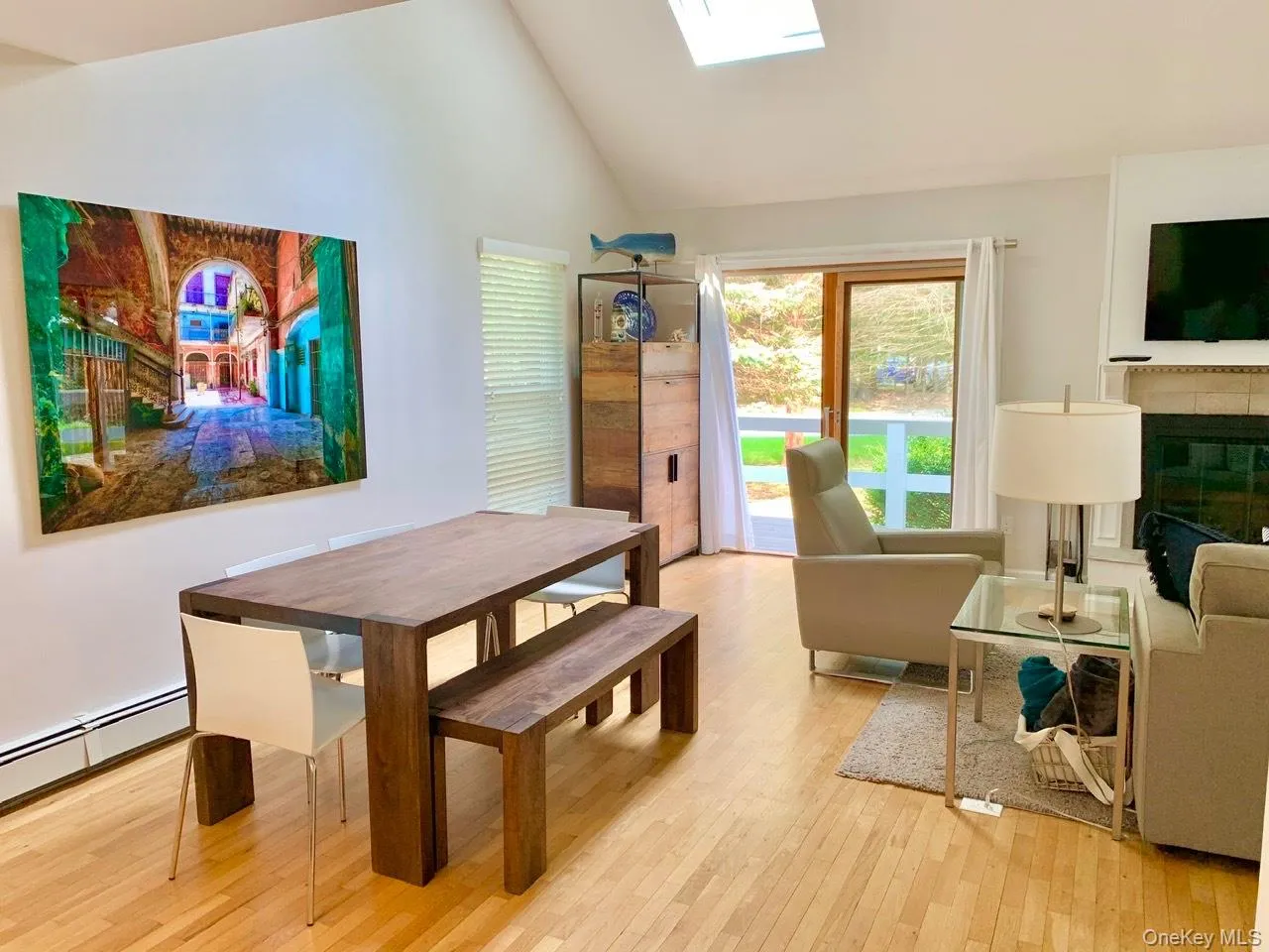 Dining space with light wood finished floors, a glass covered fireplace, a skylight, and high vaulted ceiling Dining space with light wood finished floors, a glass covered fireplace, a skylight, and high vaulted ceiling