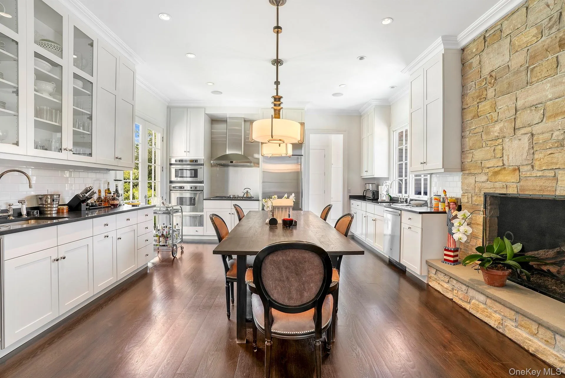 Dining room with ornamental molding, dark wood-style floors, a stone fireplace, and recessed lighting Dining room with ornamental molding, dark wood-style floors, a stone fireplace, and recessed lighting