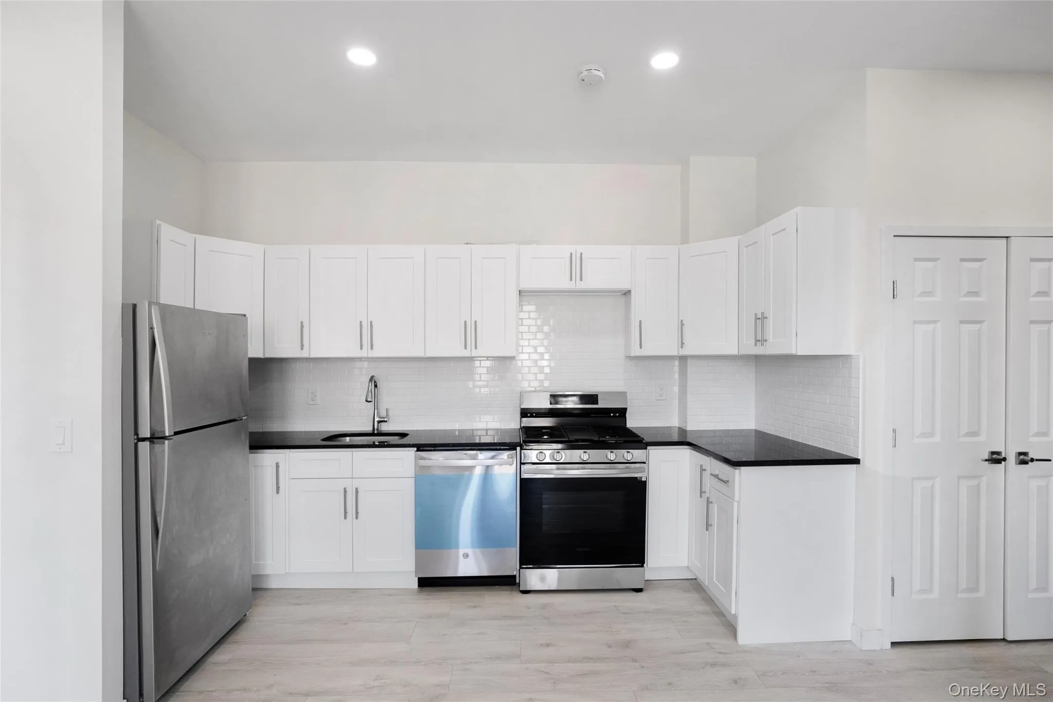 Kitchen with appliances with stainless steel finishes, white cabinetry, tasteful backsplash, light wood-type flooring, and recessed lighting Kitchen with appliances with stainless steel finishes, white cabinetry, tasteful backsplash, light wood-type flooring, and recessed lighting