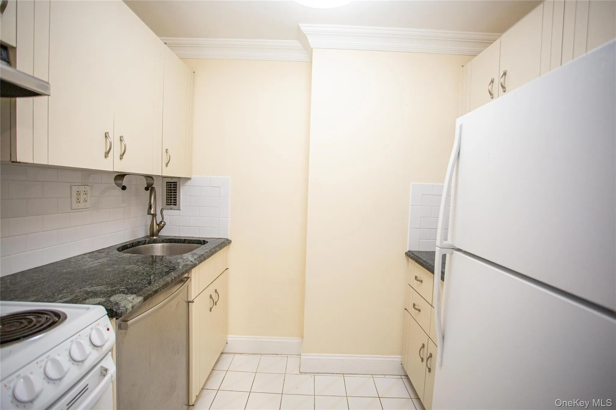 Kitchen with white appliances, tasteful backsplash, light tile patterned floors, dark stone counters, and ornamental molding Kitchen with white appliances, tasteful backsplash, light tile patterned floors, dark stone counters, and ornamental molding