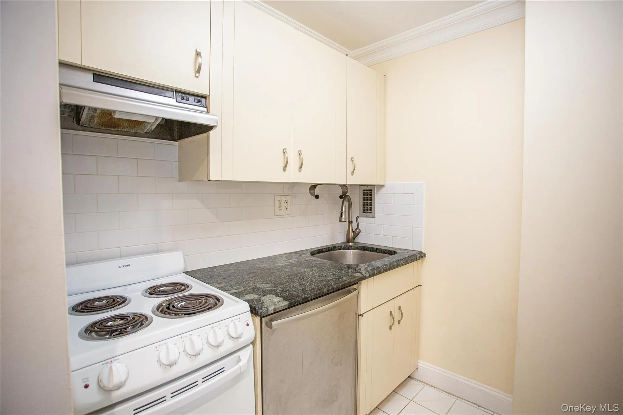 Kitchen featuring white electric range oven, tasteful backsplash, ventilation hood, stainless steel dishwasher, and light tile patterned floors Kitchen featuring white electric range oven, tasteful backsplash, ventilation hood, stainless steel dishwasher, and light tile patterned floors