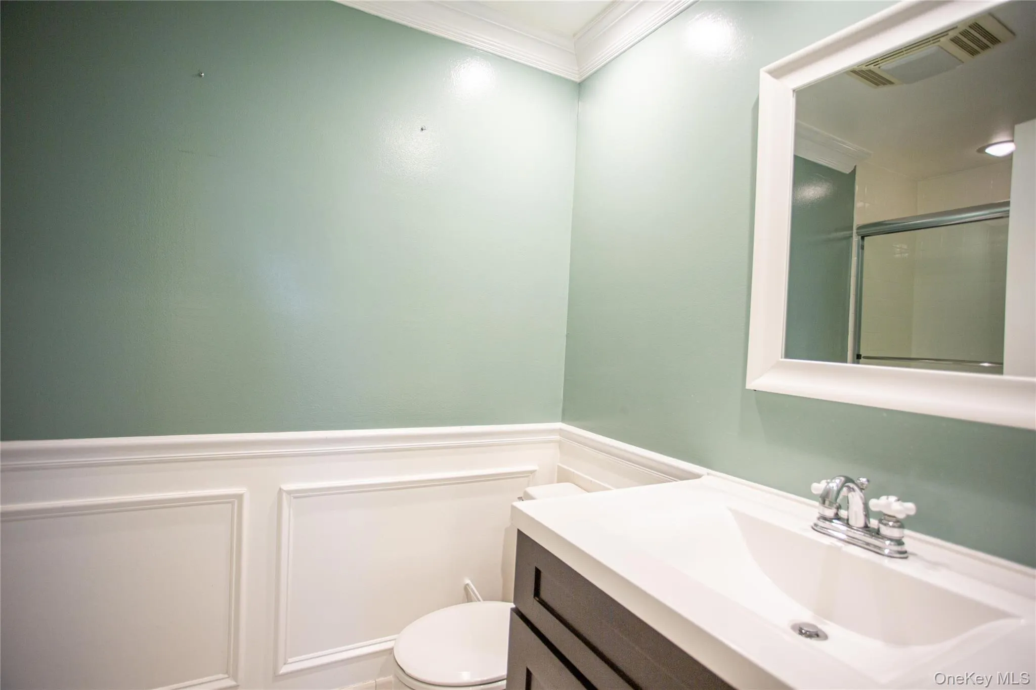 Bathroom with an enclosed shower, ornamental molding, vanity, wainscoting, and a decorative wall Bathroom with an enclosed shower, ornamental molding, vanity, wainscoting, and a decorative wall