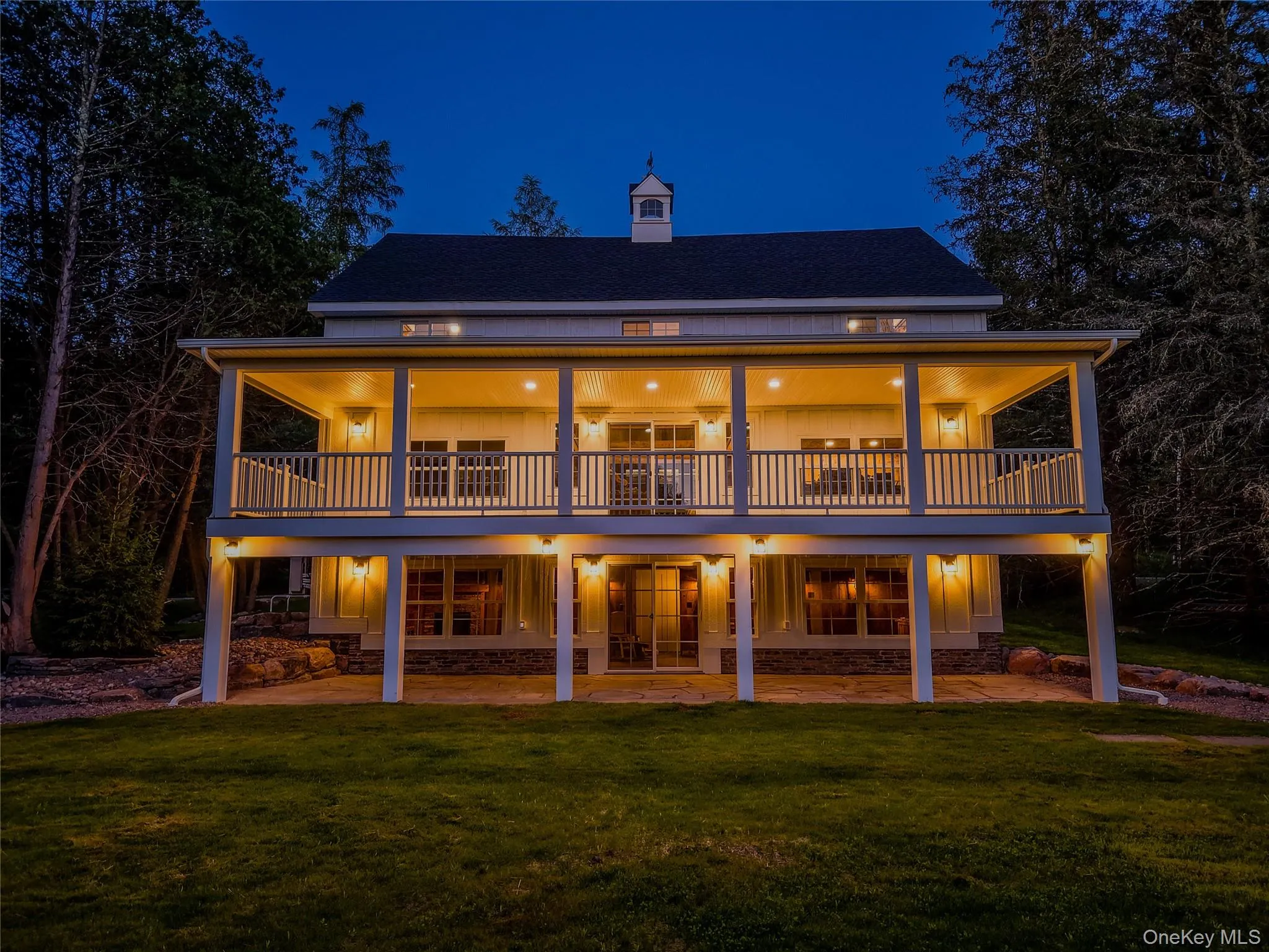 Back of house at night with a lawn, a porch, a shingled roof, and a chimney Back of house at night with a lawn, a porch, a shingled roof, and a chimney