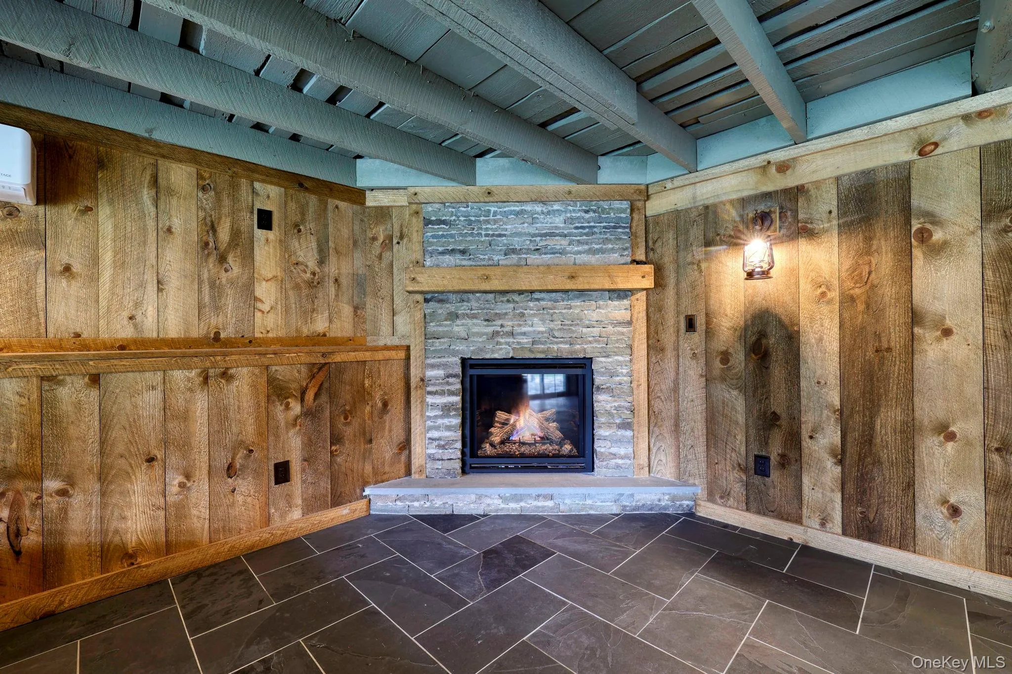 Unfurnished living room featuring beamed ceiling, wooden walls, and a stone fireplace Unfurnished living room featuring beamed ceiling, wooden walls, and a stone fireplace