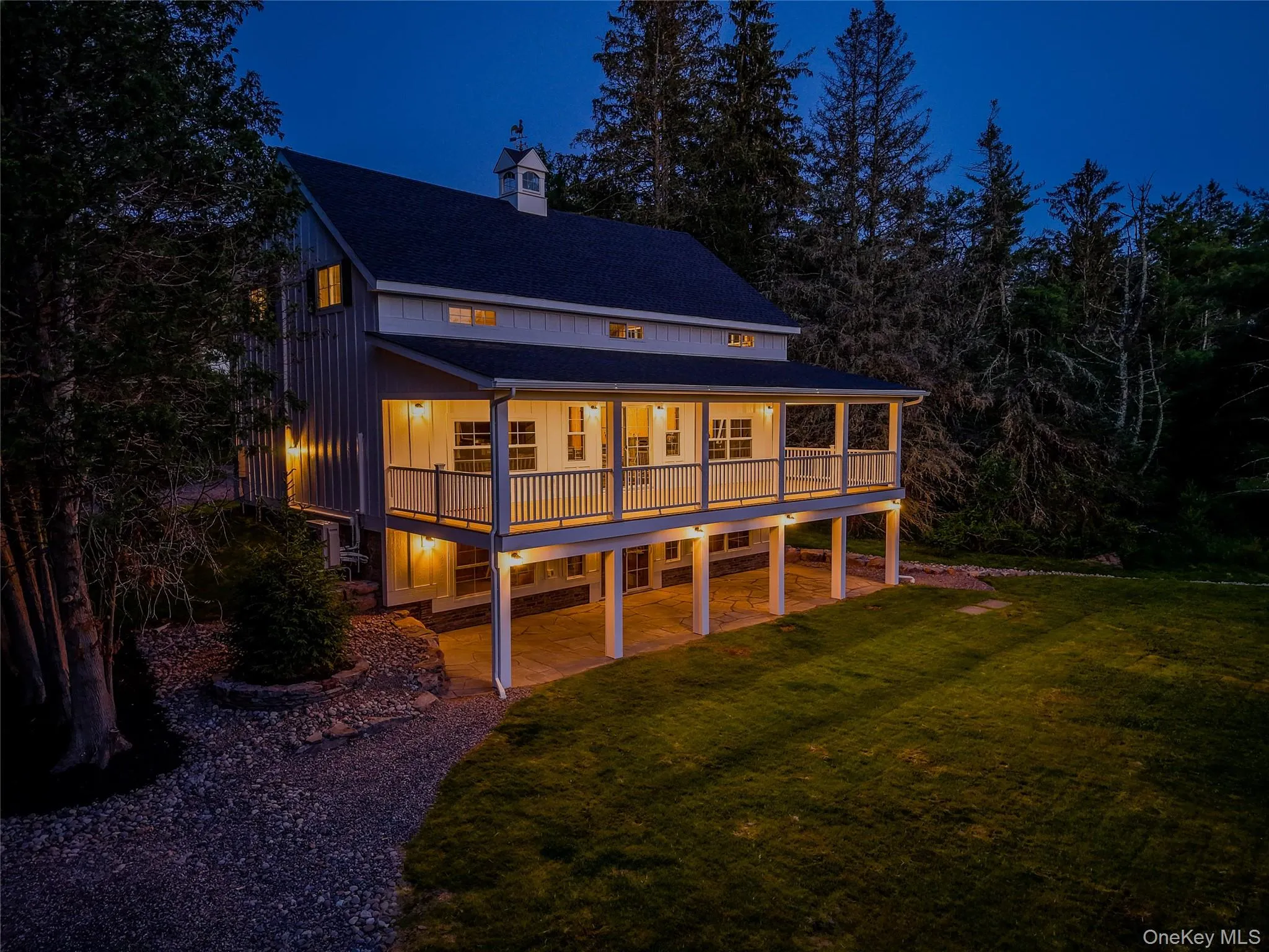 Back of house at night with a porch, a yard, board and batten siding, a shingled roof, and a chimney Back of house at night with a porch, a yard, board and batten siding, a shingled roof, and a chimney