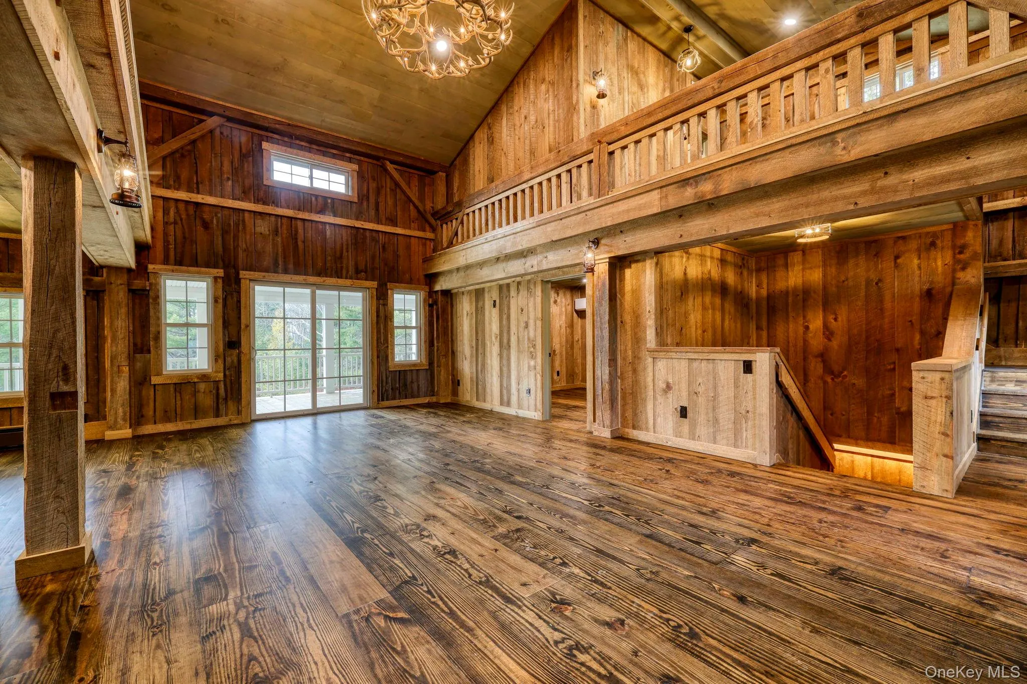 Unfurnished living room with high vaulted ceiling, wooden walls, dark wood-type flooring, wooden ceiling, and a chandelier Unfurnished living room with high vaulted ceiling, wooden walls, dark wood-type flooring, wooden ceiling, and a chandelier