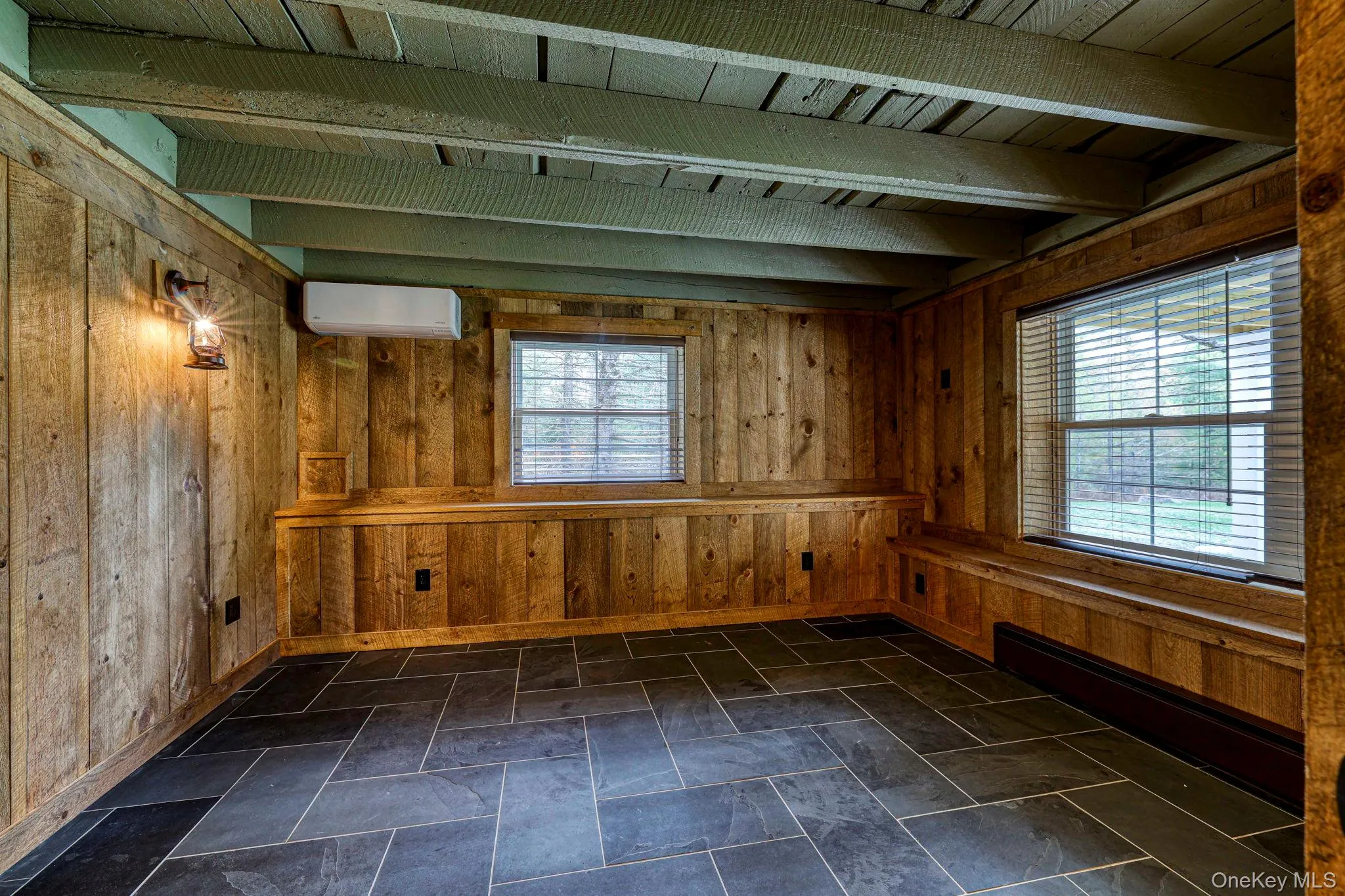 Empty room with a baseboard radiator, wooden walls, beam ceiling, and a wall mounted air conditioner Empty room with a baseboard radiator, wooden walls, beam ceiling, and a wall mounted air conditioner