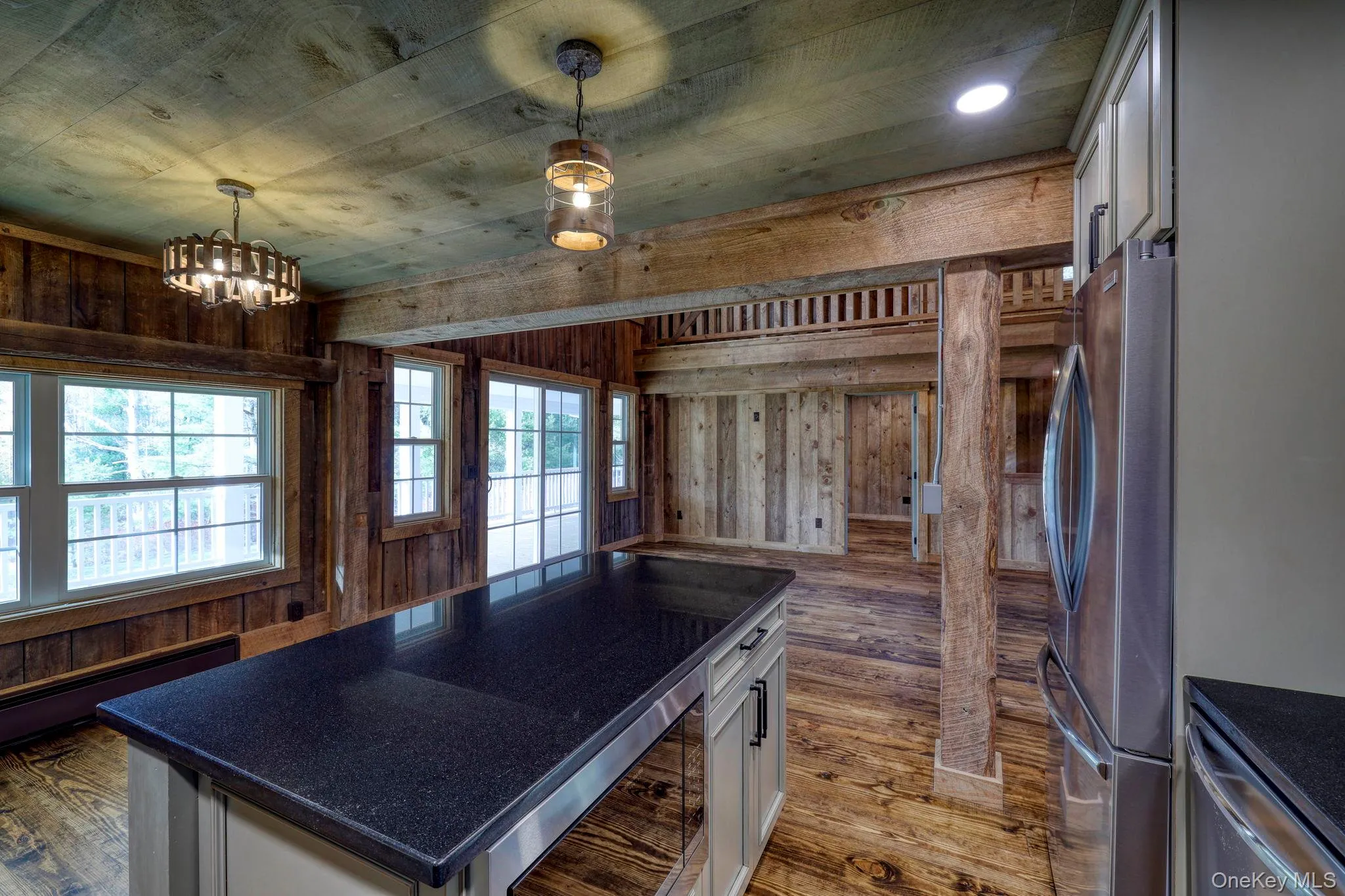Kitchen with white cabinetry, hanging light fixtures, dark wood-type flooring, appliances with stainless steel finishes, and wooden walls Kitchen with white cabinetry, hanging light fixtures, dark wood-type flooring, appliances with stainless steel finishes, and wooden walls