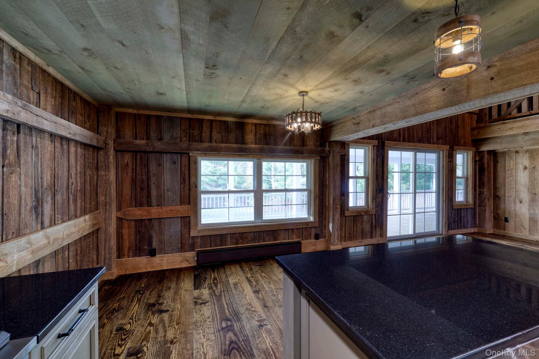 Kitchen with white cabinets, wood walls, baseboard heating, plenty of natural light, and pendant lighting Kitchen with white cabinets, wood walls, baseboard heating, plenty of natural light, and pendant lighting