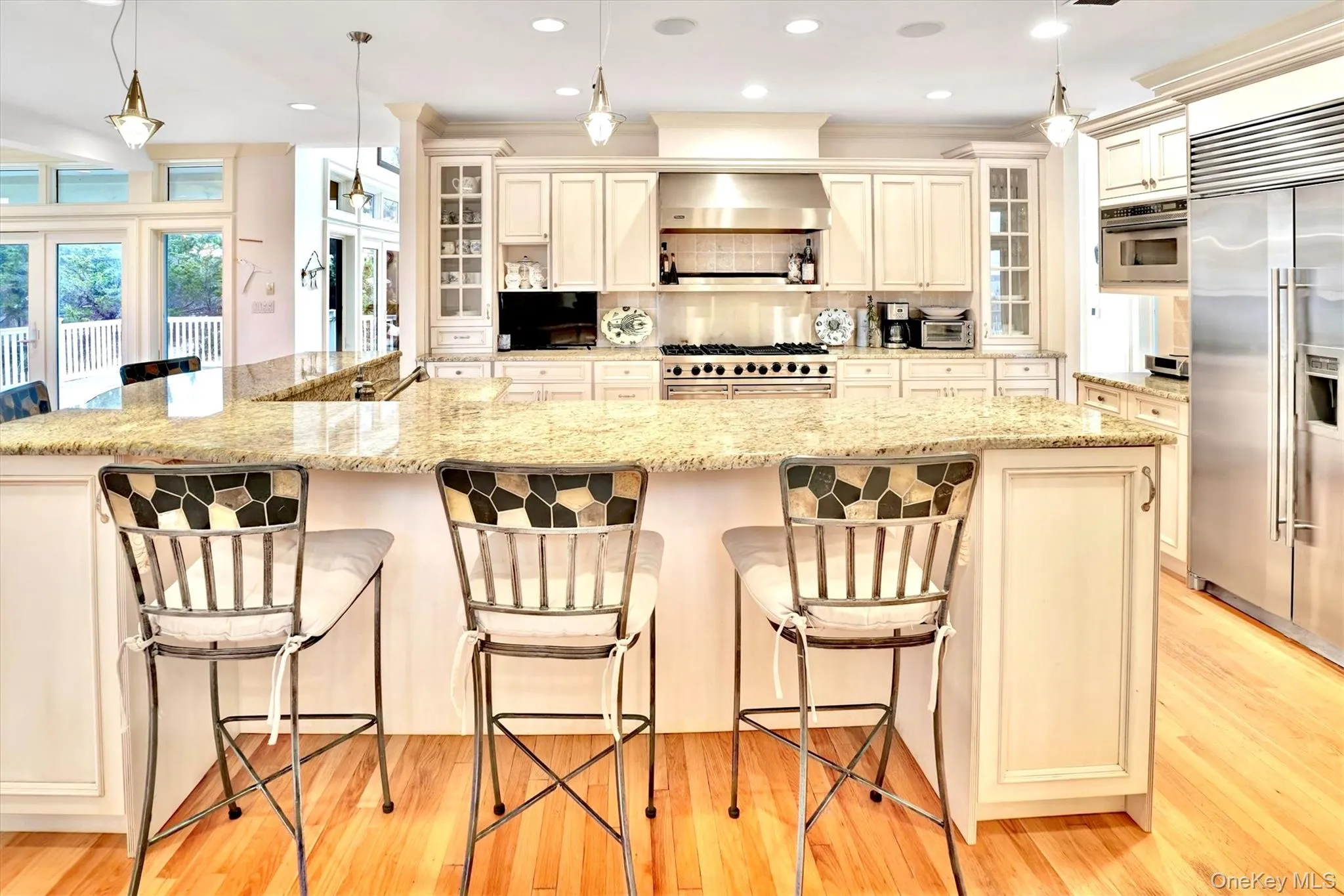 Kitchen featuring decorative light fixtures, cream cabinetry, premium appliances, recessed lighting, and light stone countertops. Subzero refrigerator and freezer.