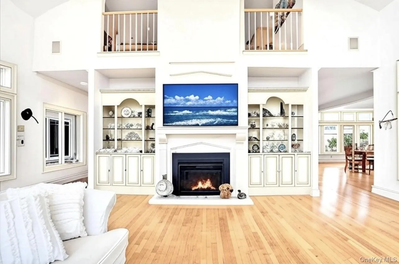Living area featuring hardwood / wood-style flooring, a glass covered fireplace, high vaulted ceiling, and built in shelves