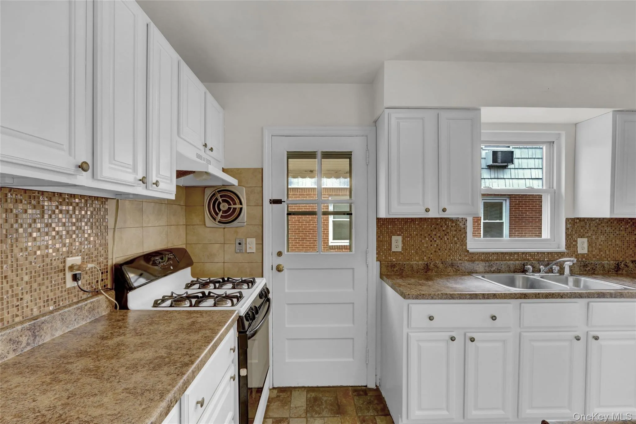 Kitchen featuring white cabinetry, gas range, and decorative backsplash Kitchen featuring white cabinetry, gas range, and decorative backsplash