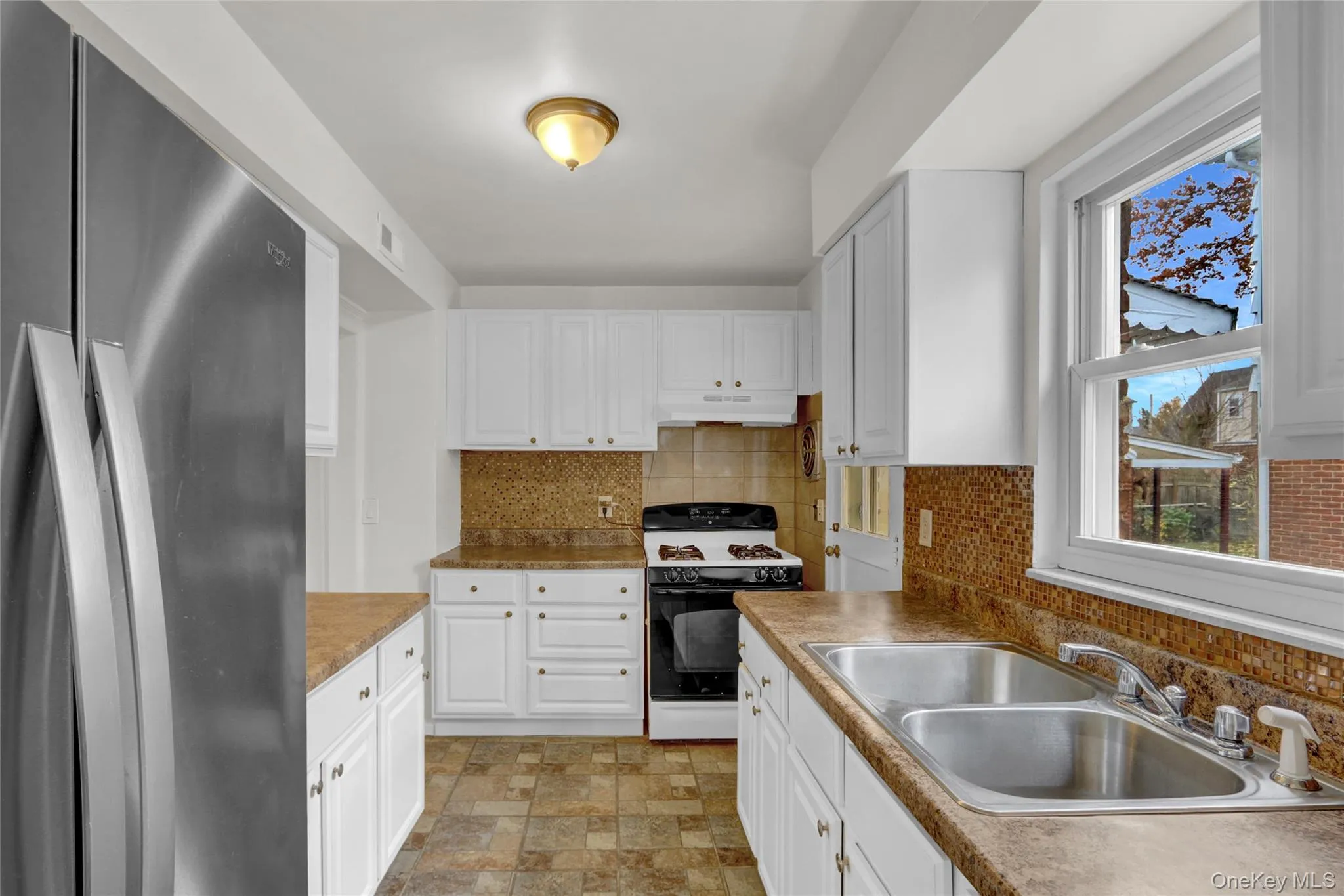 Kitchen featuring freestanding refrigerator, gas range oven, white cabinetry and backsplash Kitchen featuring freestanding refrigerator, gas range oven, white cabinetry and backsplash