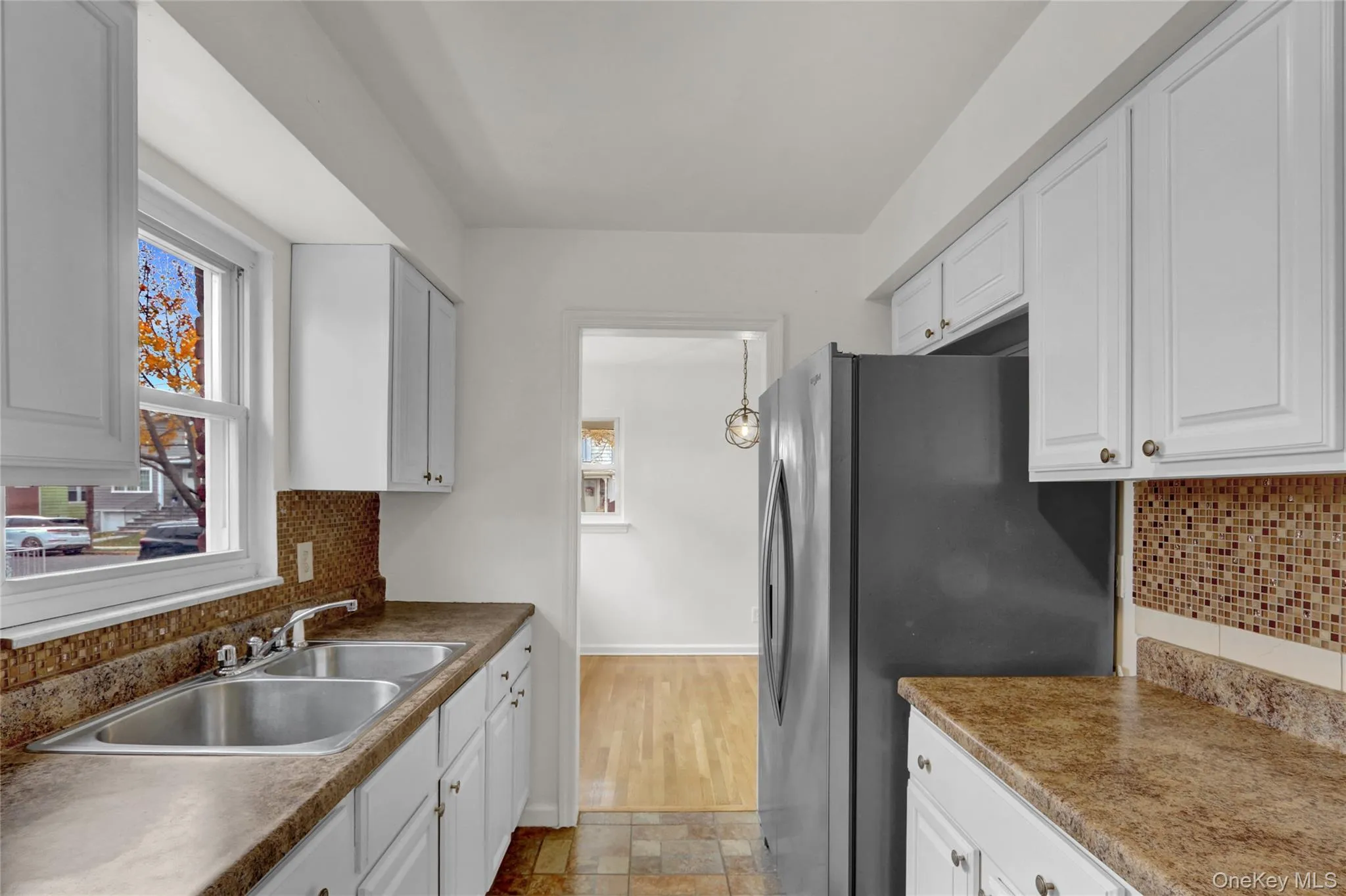 Kitchen featuring backsplash, freestanding refrigerator, stone tile floors, and white cabinetry Kitchen featuring backsplash, freestanding refrigerator, stone tile floors, and white cabinetry