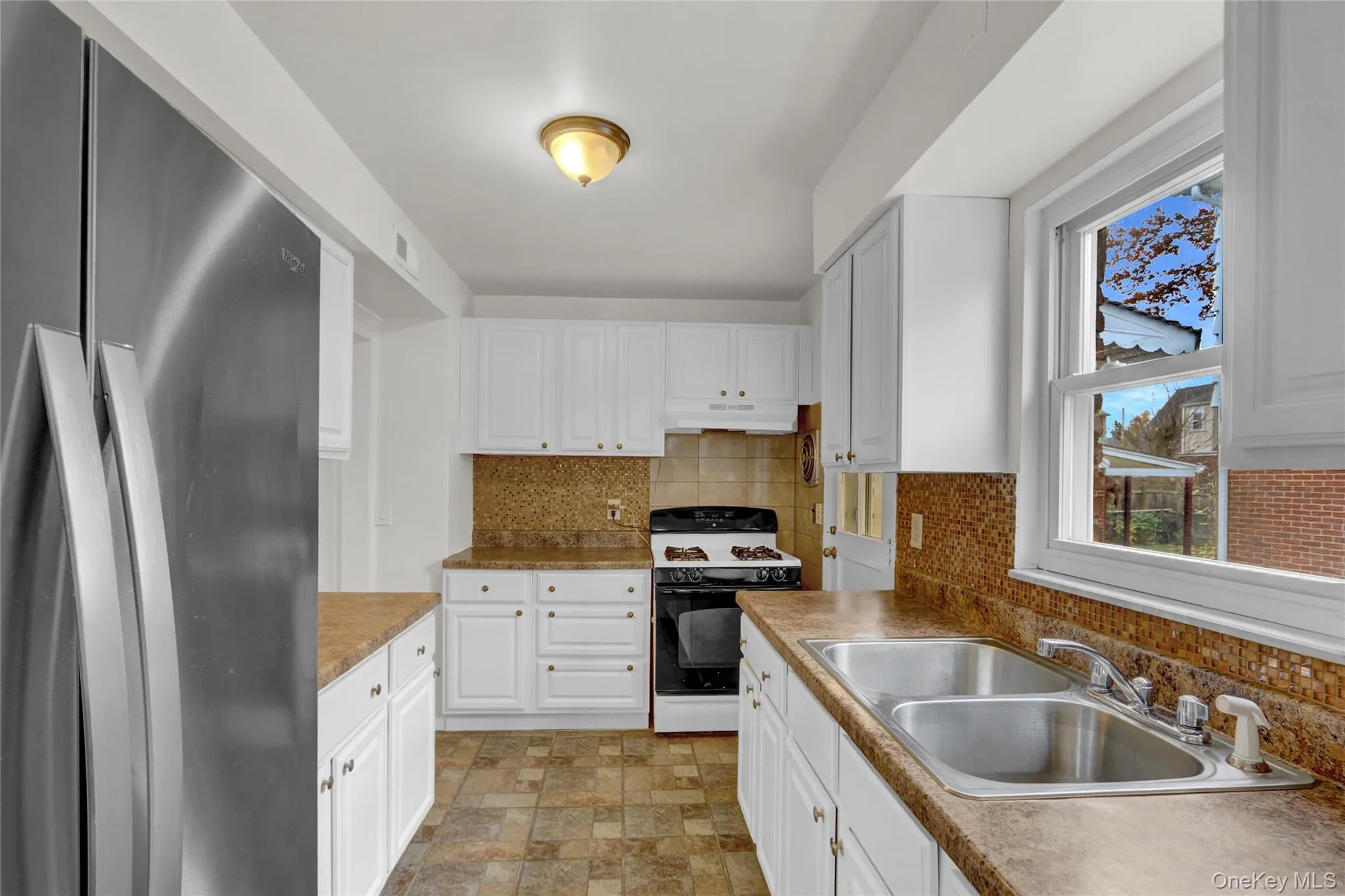 Kitchen with freestanding refrigerator, gas range, tasteful backsplash, white cabinetry Kitchen with freestanding refrigerator, gas range, tasteful backsplash, white cabinetry