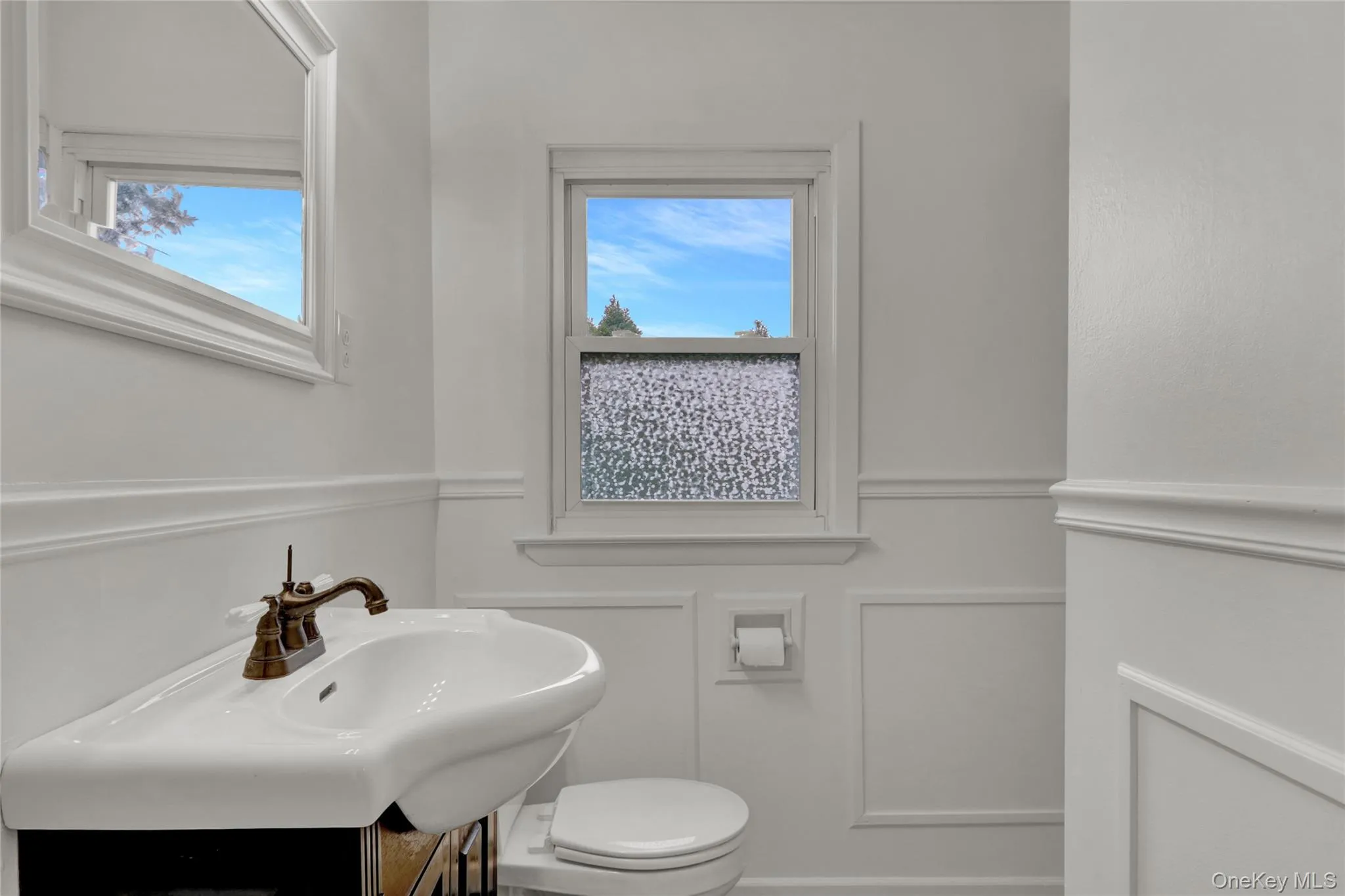 Half bath featuring a decorative wall, a wainscoted wall, vanity, and plenty of natural light Half bath featuring a decorative wall, a wainscoted wall, vanity, and plenty of natural light