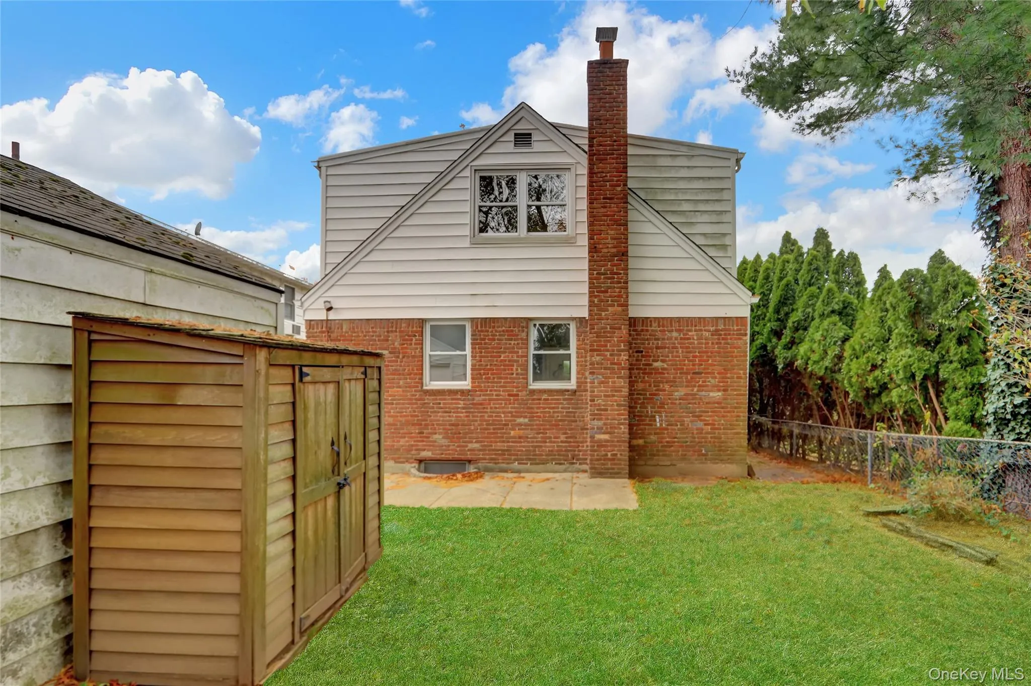 Back of house featuring a chimney, a fenced backyard, brick siding, a storage shed, and a patio area Back of house featuring a chimney, a fenced backyard, brick siding, a storage shed, and a patio area