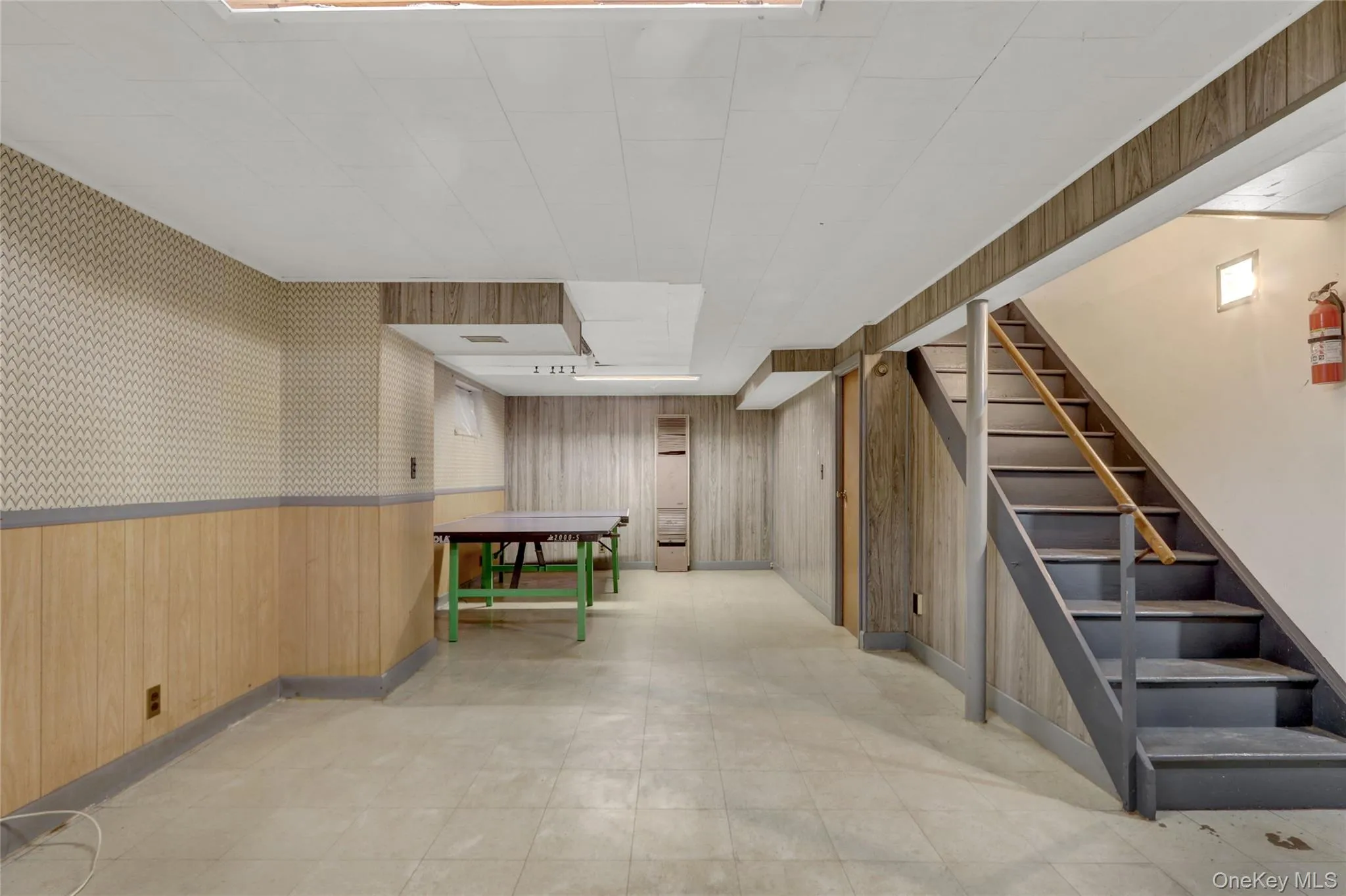 Finished below grade area featuring wood walls, wallpapered walls, wainscoting, stairway, and light floors Finished below grade area featuring wood walls, wallpapered walls, wainscoting, stairway, and light floors