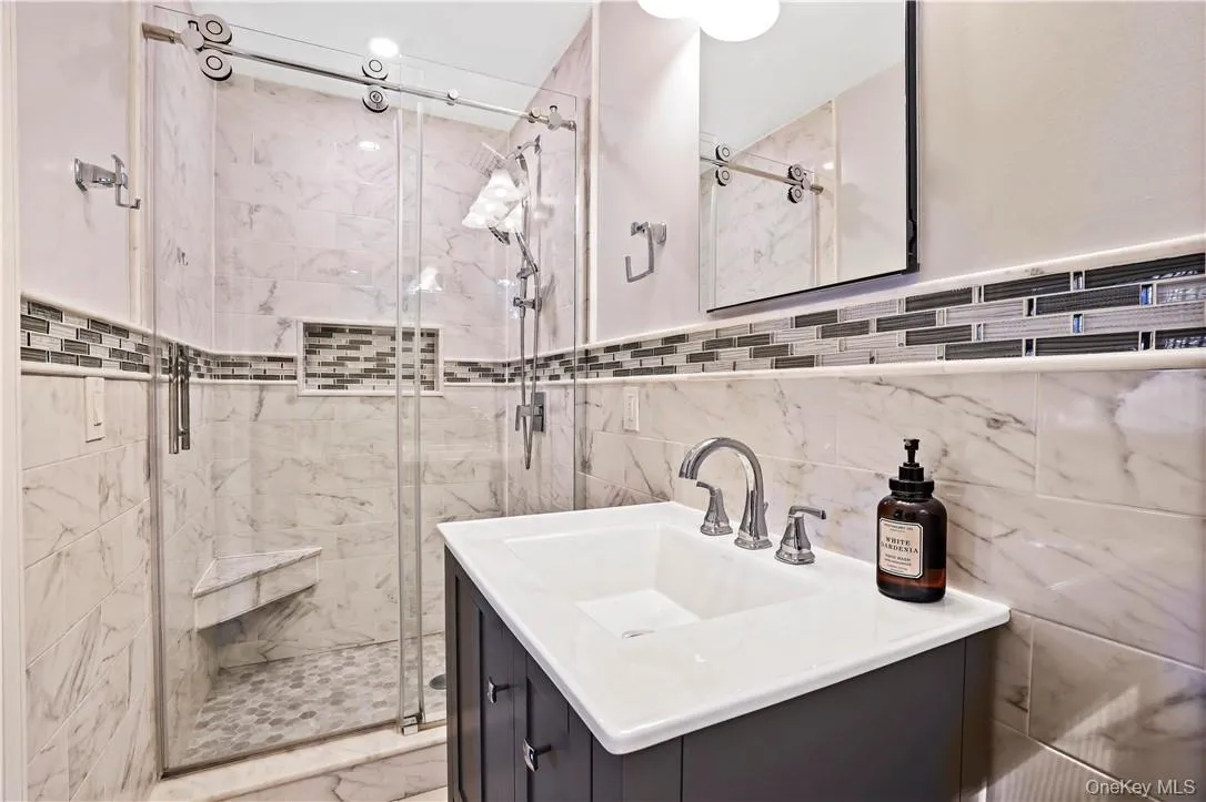 Bathroom featuring tasteful backsplash, a shower with door, tile walls, and large vanity Bathroom featuring tasteful backsplash, a shower with door, tile walls, and large vanity