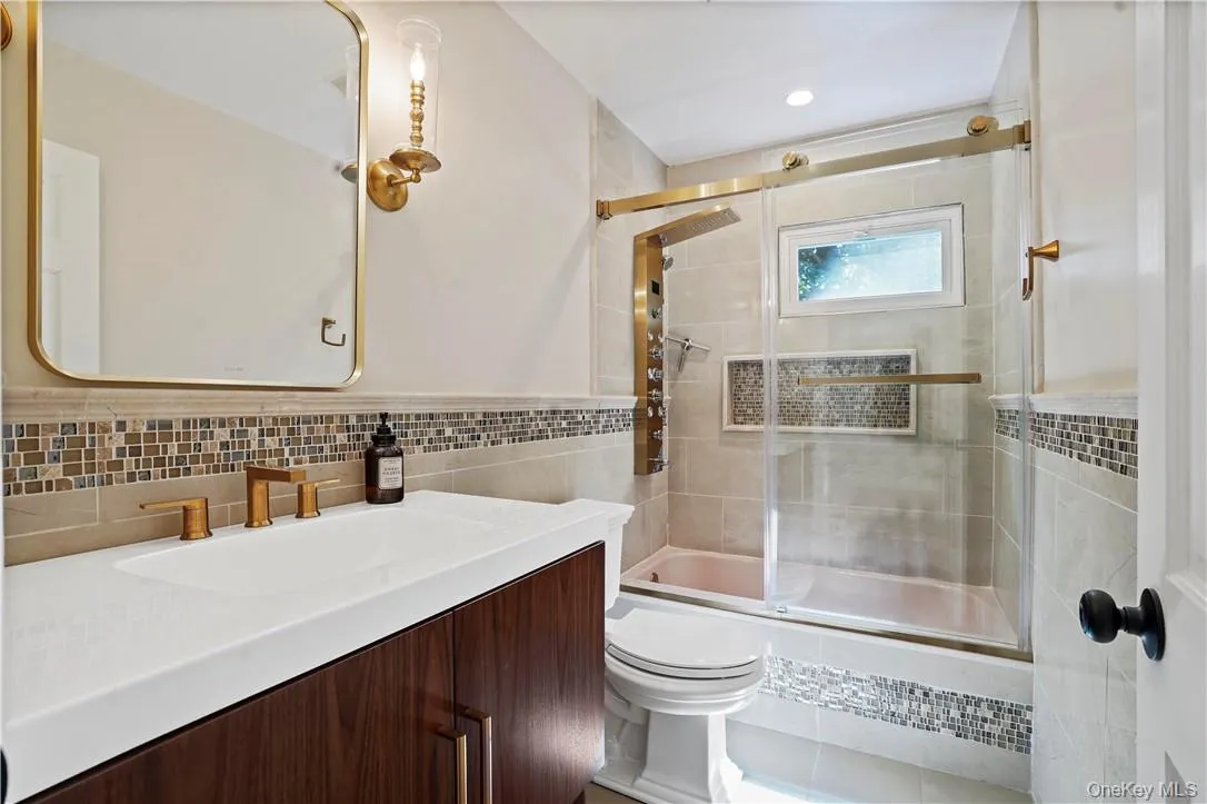 Full bathroom featuring shower / bath combination with glass door, tile walls, toilet, tasteful backsplash, and vanity Full bathroom featuring shower / bath combination with glass door, tile walls, toilet, tasteful backsplash, and vanity