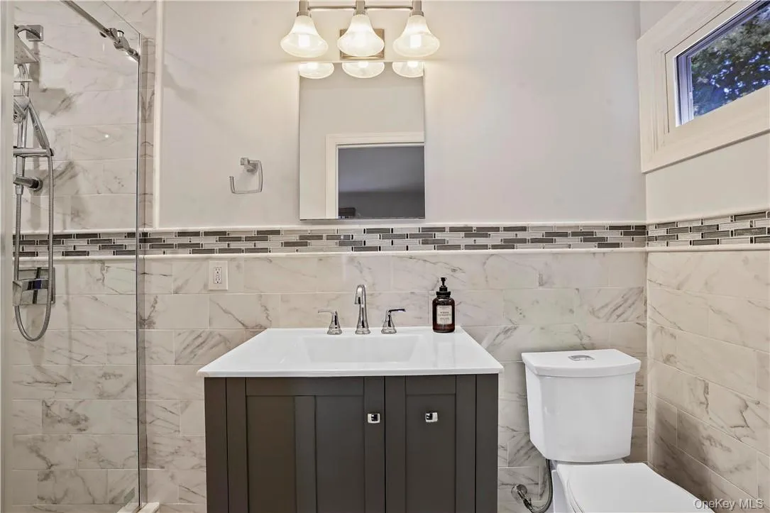 Bathroom with backsplash, tile walls, toilet, and vanity Bathroom with backsplash, tile walls, toilet, and vanity