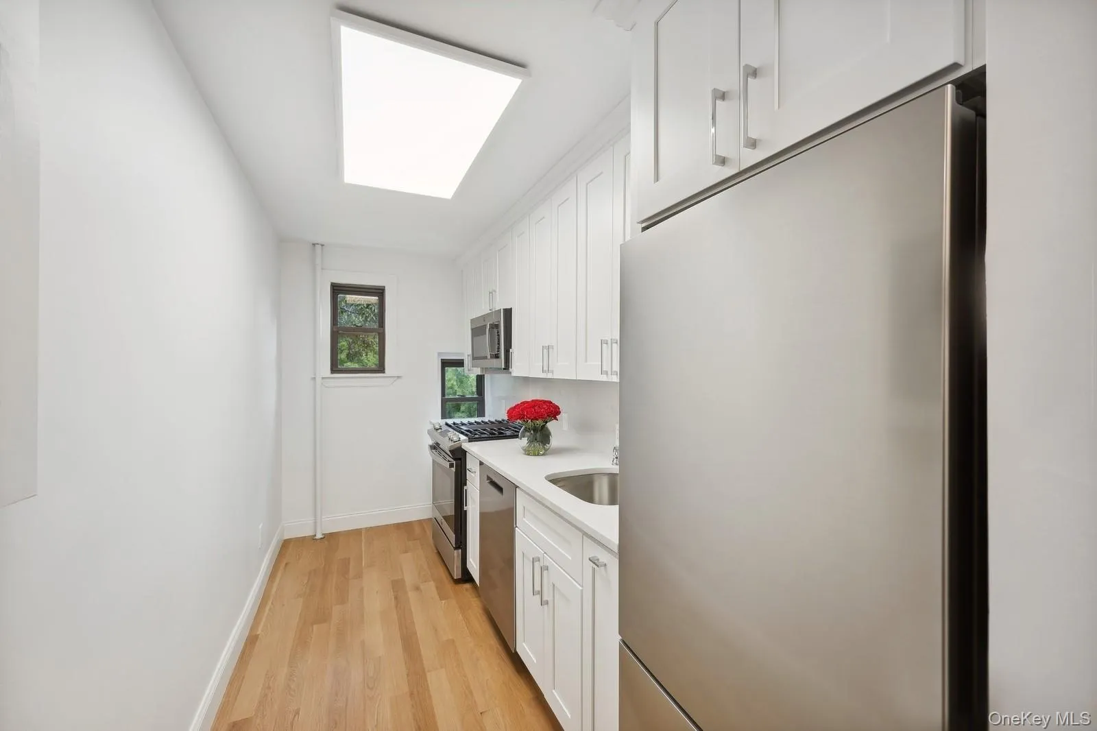 Kitchen featuring stainless steel appliances, white cabinets, light wood-style floors, and light stone counters Kitchen featuring stainless steel appliances, white cabinets, light wood-style floors, and light stone counters