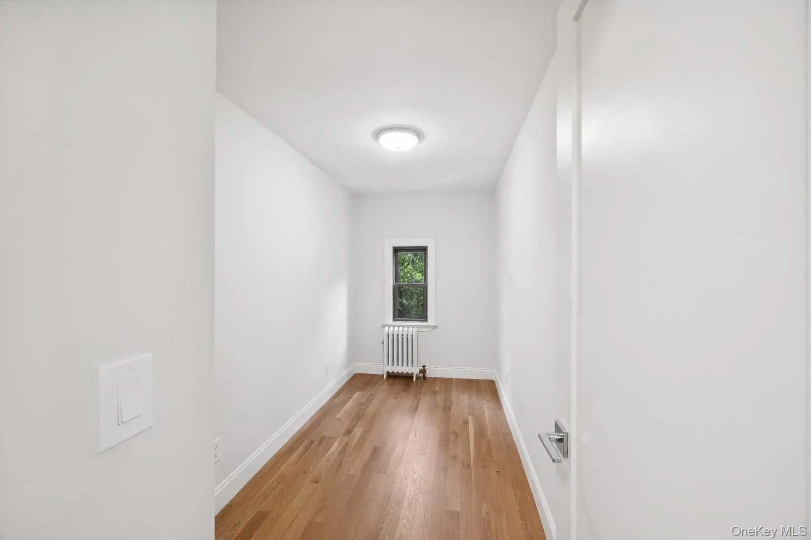 Empty room with light wood-style flooring and radiator heating unit Empty room with light wood-style flooring and radiator heating unit