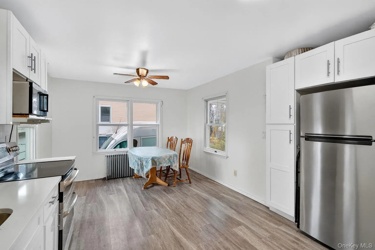 Kitchen featuring stainless steel appliances, white cabinets, light wood finished floors, and radiator heating unit Kitchen featuring stainless steel appliances, white cabinets, light wood finished floors, and radiator heating unit