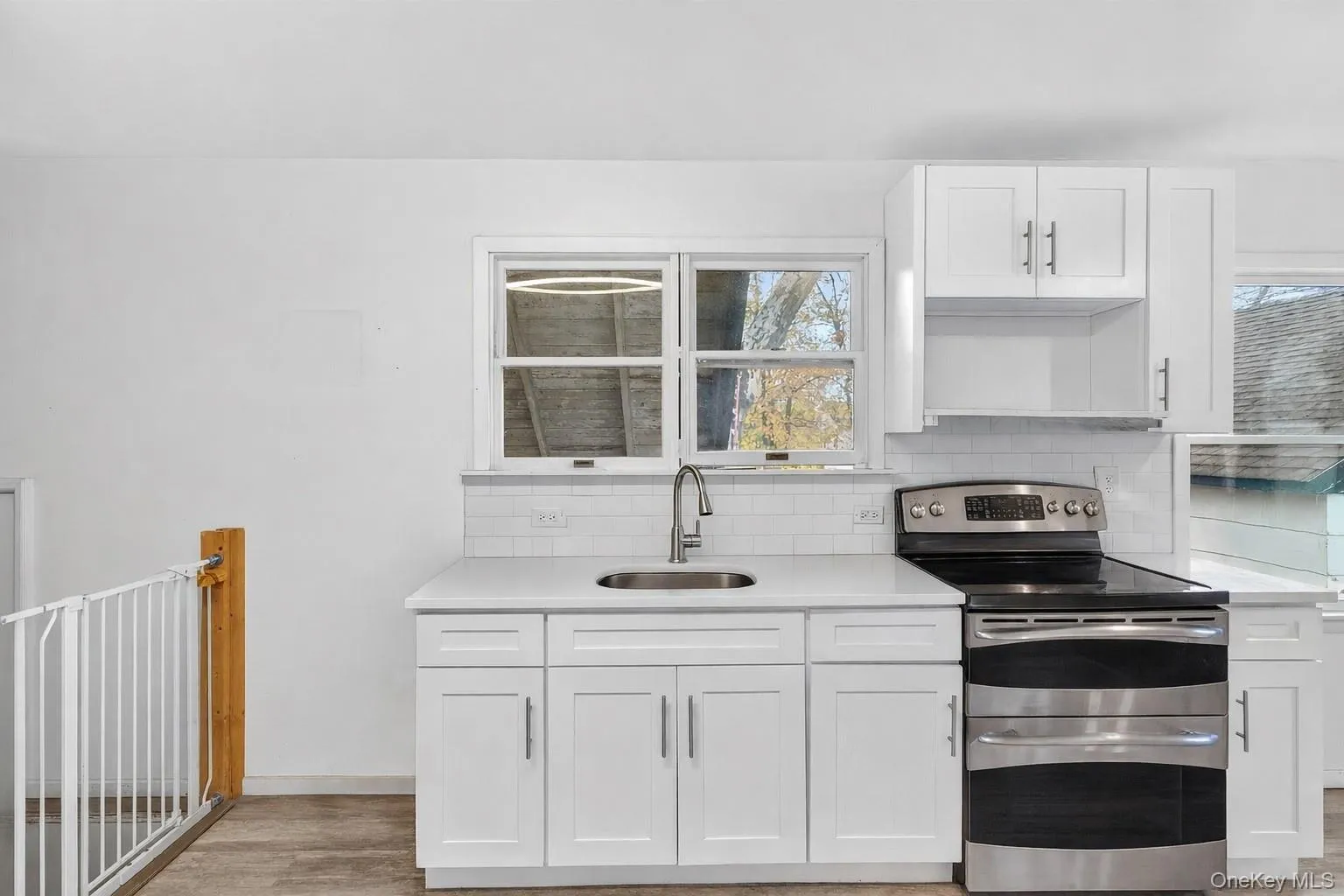Kitchen featuring double oven range, white cabinetry, decorative backsplash, light stone countertops, and light wood-style flooring Kitchen featuring double oven range, white cabinetry, decorative backsplash, light stone countertops, and light wood-style flooring