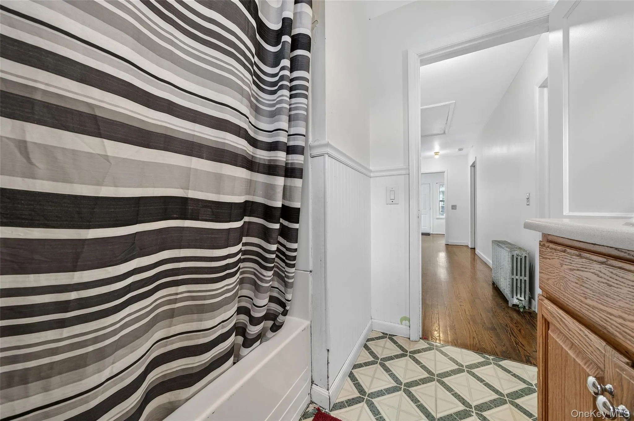 Full bathroom with shower / bathtub combination with curtain, radiator heating unit, vanity, inlaid floor details, and light tile patterned floors Full bathroom with shower / bathtub combination with curtain, radiator heating unit, vanity, inlaid floor details, and light tile patterned floors