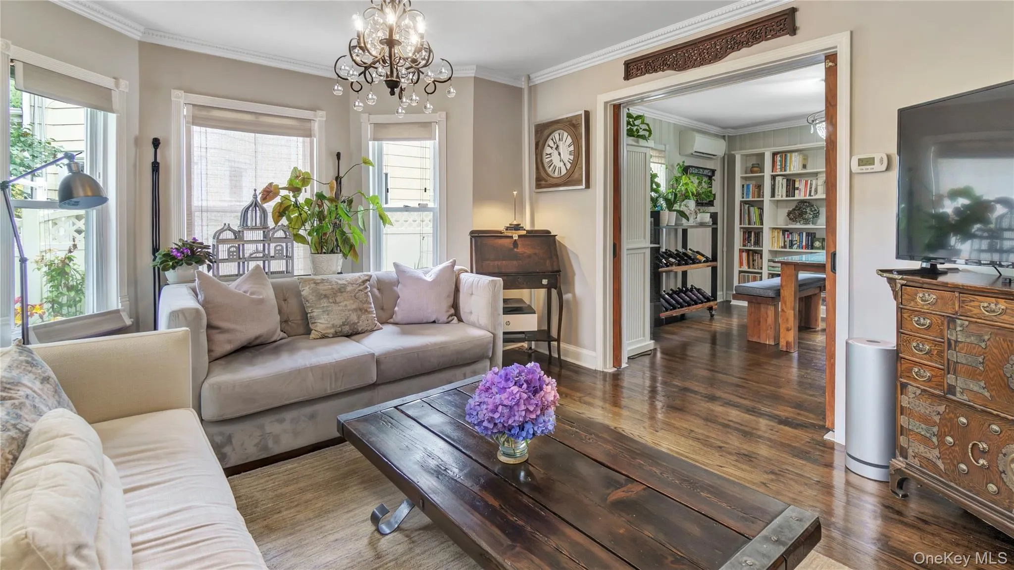 Living room with ornamental molding, wood finished floors, healthy amount of natural light, a chandelier, and a wall mounted AC Living room with ornamental molding, wood finished floors, healthy amount of natural light, a chandelier, and a wall mounted AC