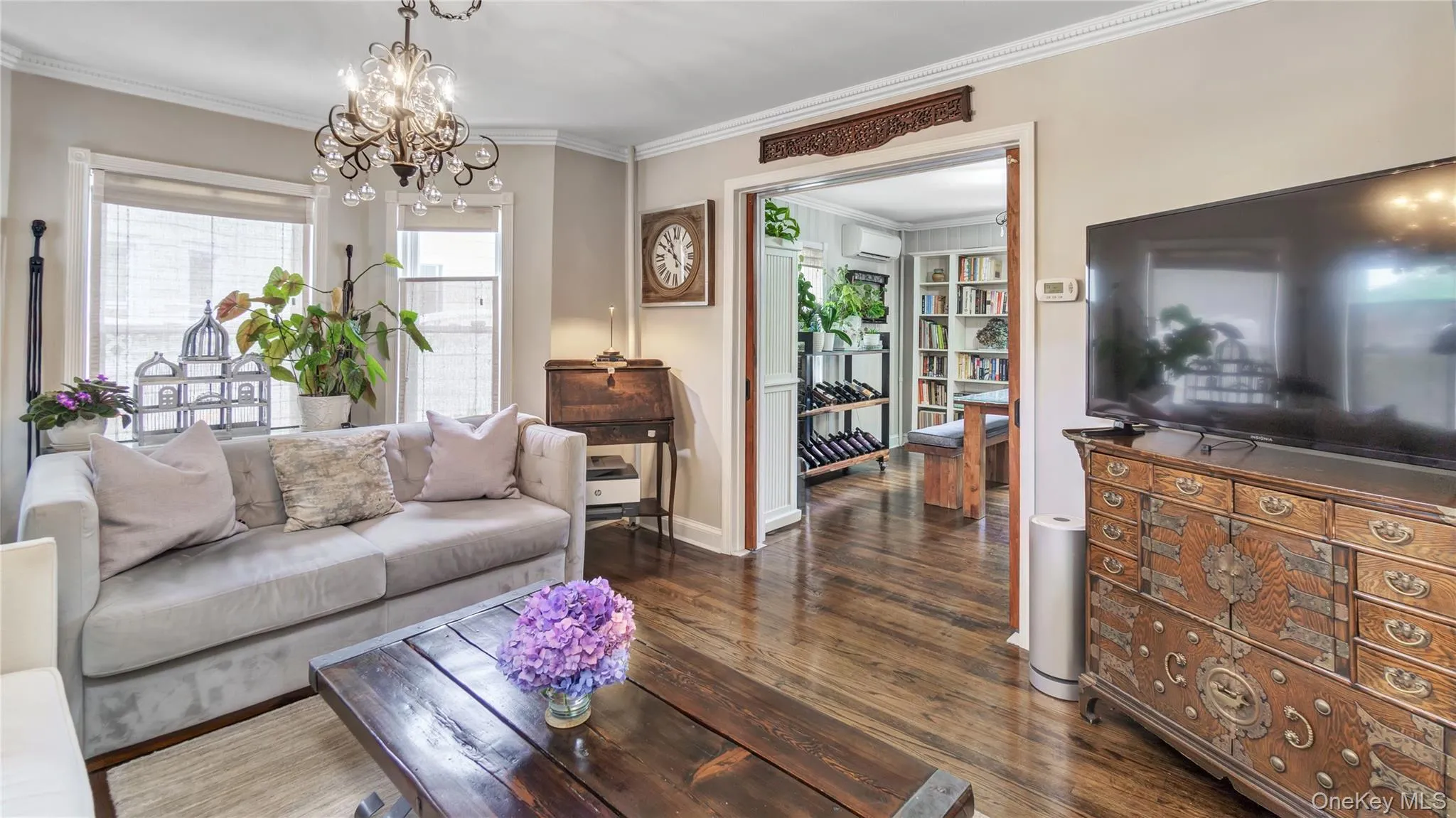 Living room featuring crown molding, dark wood-type flooring, healthy amount of natural light, an AC wall unit, and a chandelier Living room featuring crown molding, dark wood-type flooring, healthy amount of natural light, an AC wall unit, and a chandelier