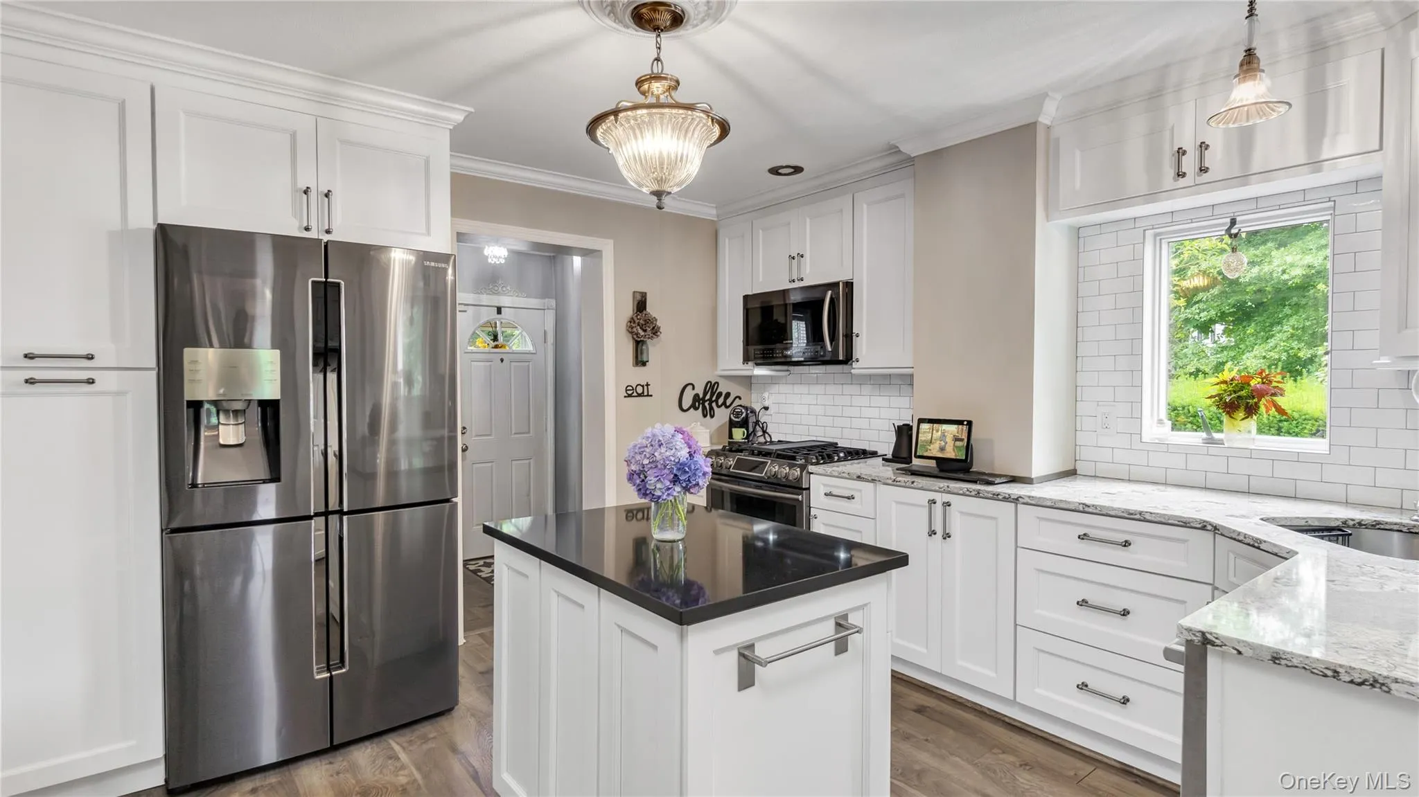Kitchen featuring white cabinets, appliances with stainless steel finishes, dark stone counters, ornamental molding, and tasteful backsplash Kitchen featuring white cabinets, appliances with stainless steel finishes, dark stone counters, ornamental molding, and tasteful backsplash