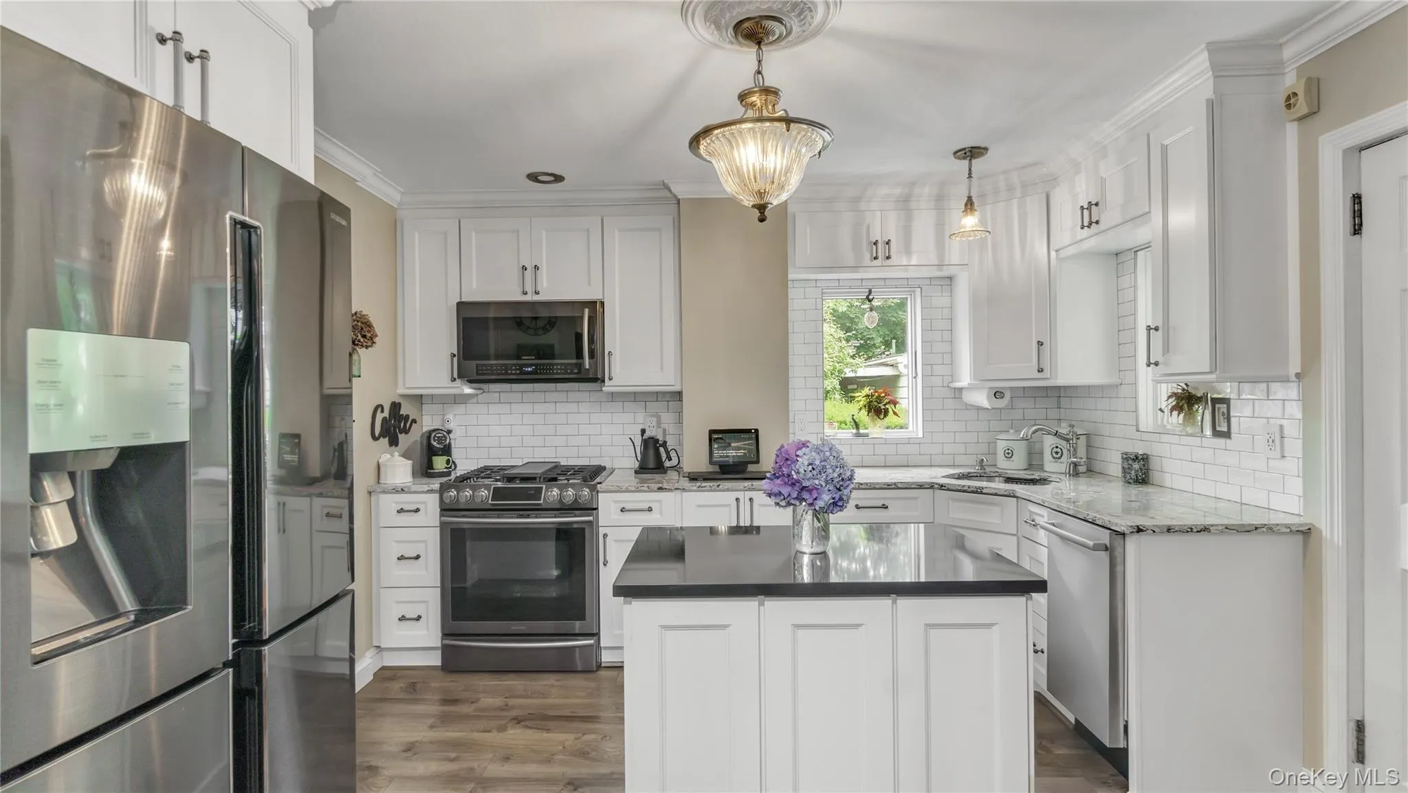 Kitchen featuring stainless steel appliances, dark stone countertops, dark wood-type flooring, white cabinetry, and ornamental molding Kitchen featuring stainless steel appliances, dark stone countertops, dark wood-type flooring, white cabinetry, and ornamental molding